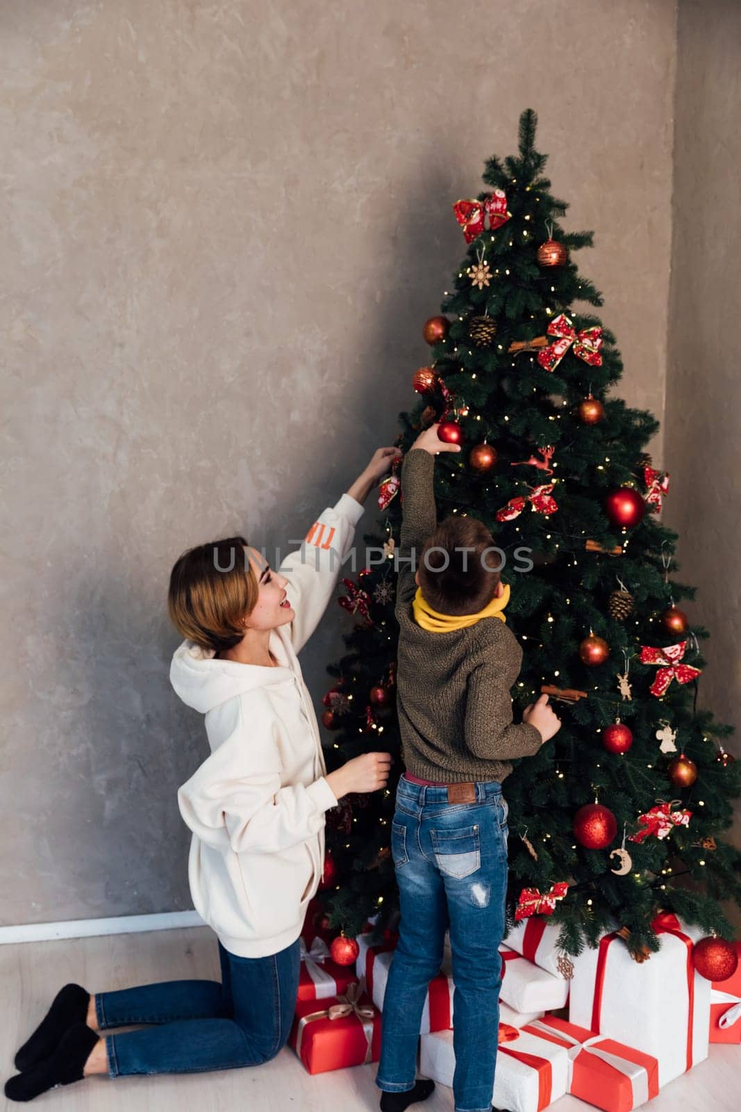 mother and son decorate the Christmas tree for the holiday New Year Christmas by Simakov