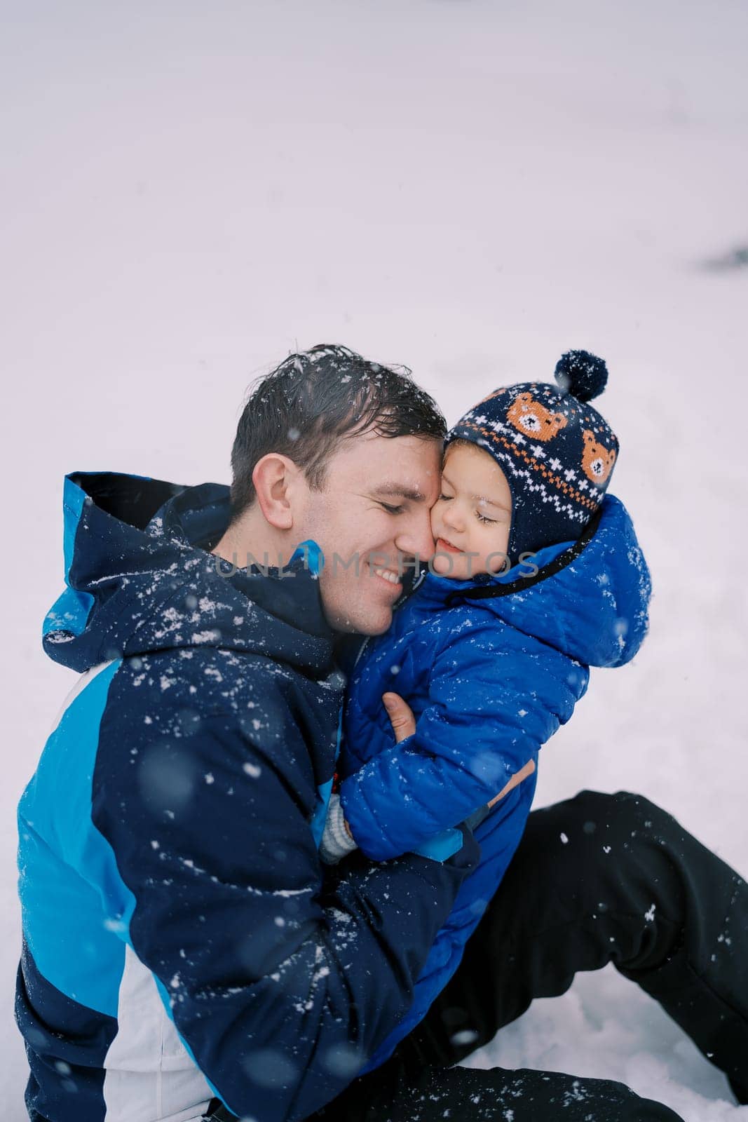 Dad hugs a little girl sitting in the snow under a snowfall. High quality photo