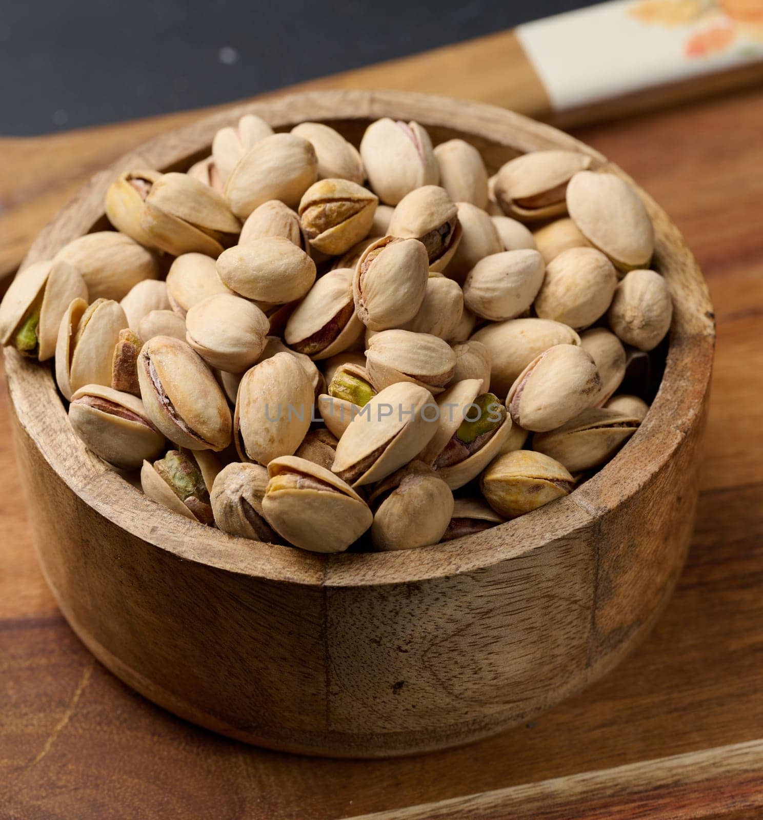 Salted roasted pistachios in a wooden round bowl on the table