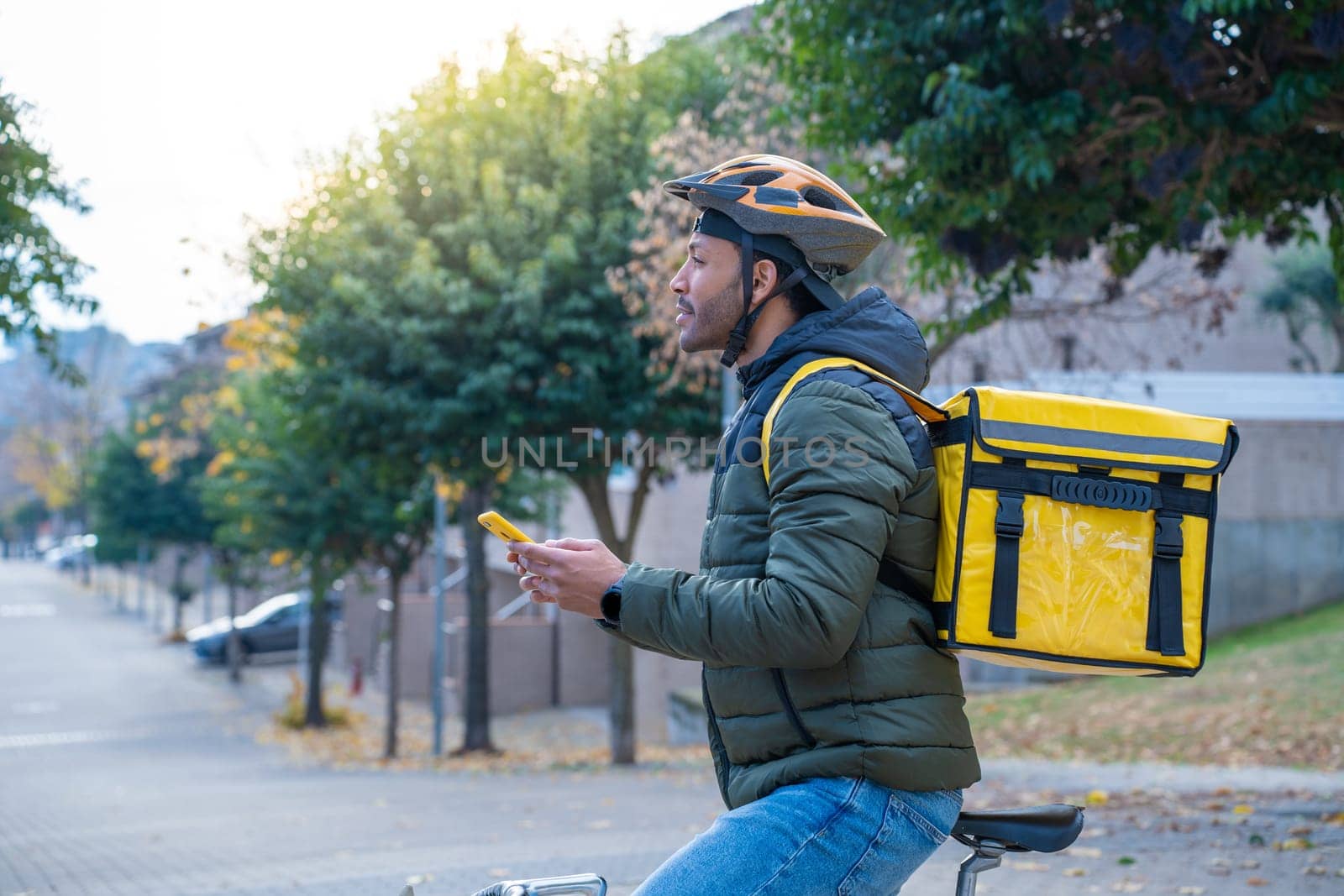 Delivery man on bike looking GPS location in the phone. Black courier delivering food and drink. by PaulCarr