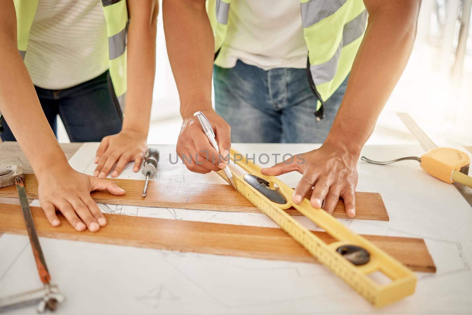 Adding some texture to the home. two unrecognisable construction workers standing together and using a ruler to measure a beam of wood. by YuriArcurs