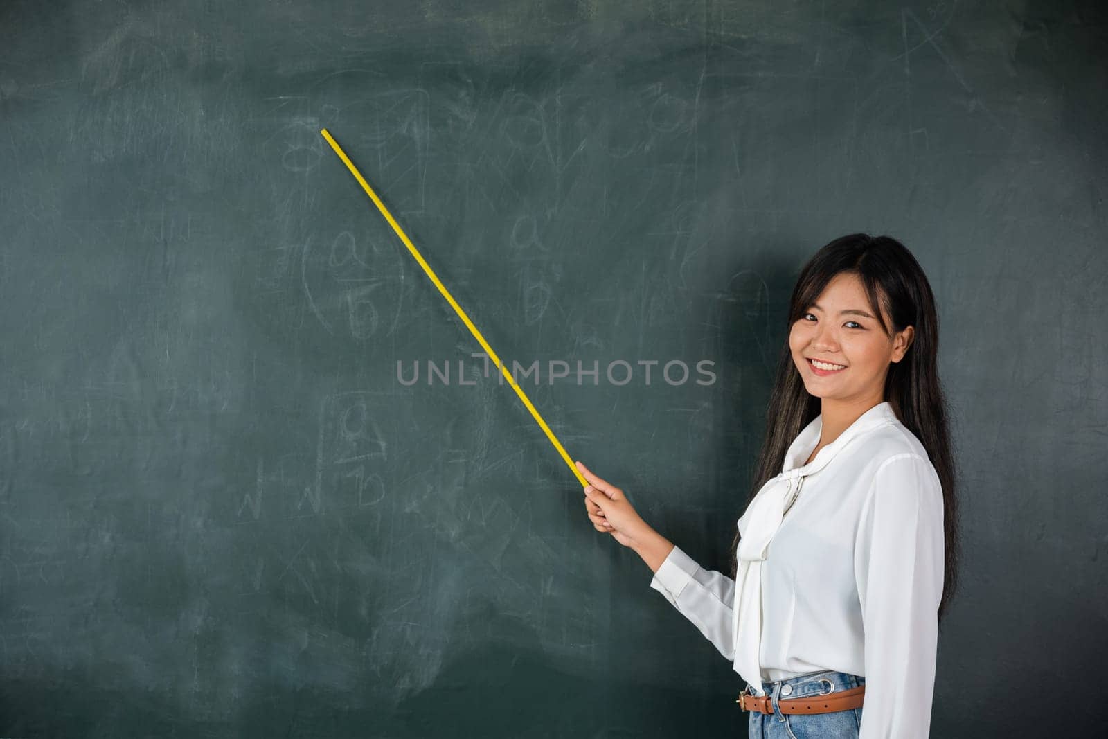 Asian female teacher smiling with wooden stick pointing to blackboard by Sorapop
