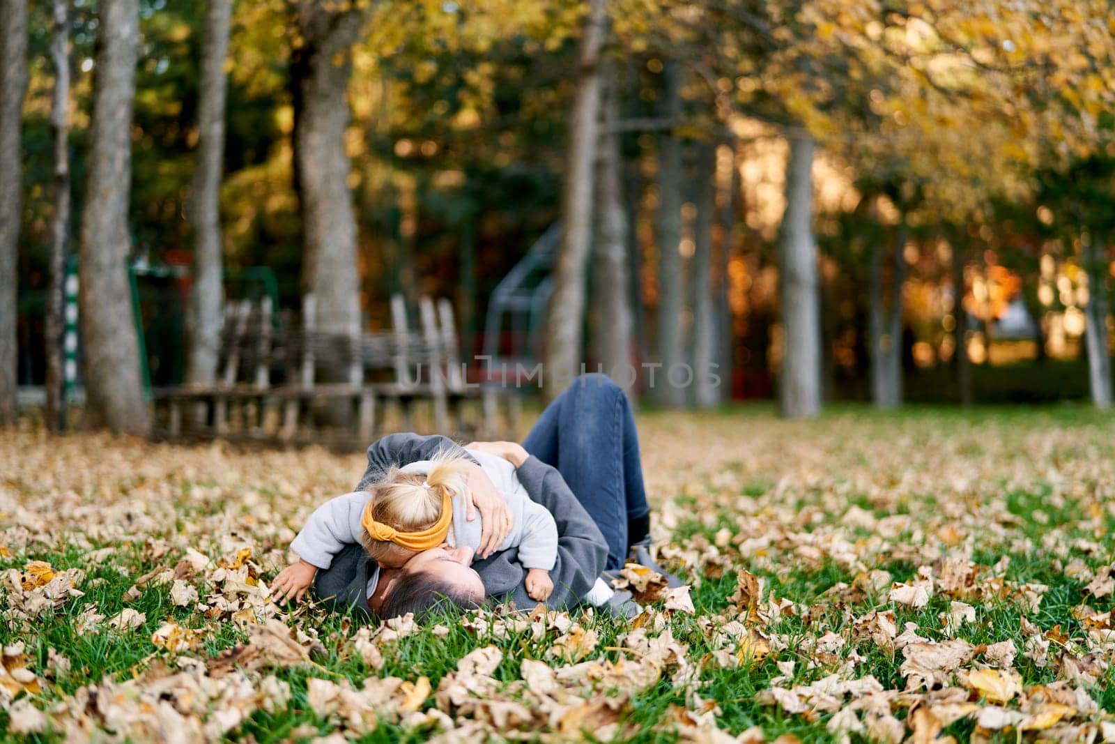 Little girl lies on her mother stomach on the autumn lawn, hugging her. High quality photo