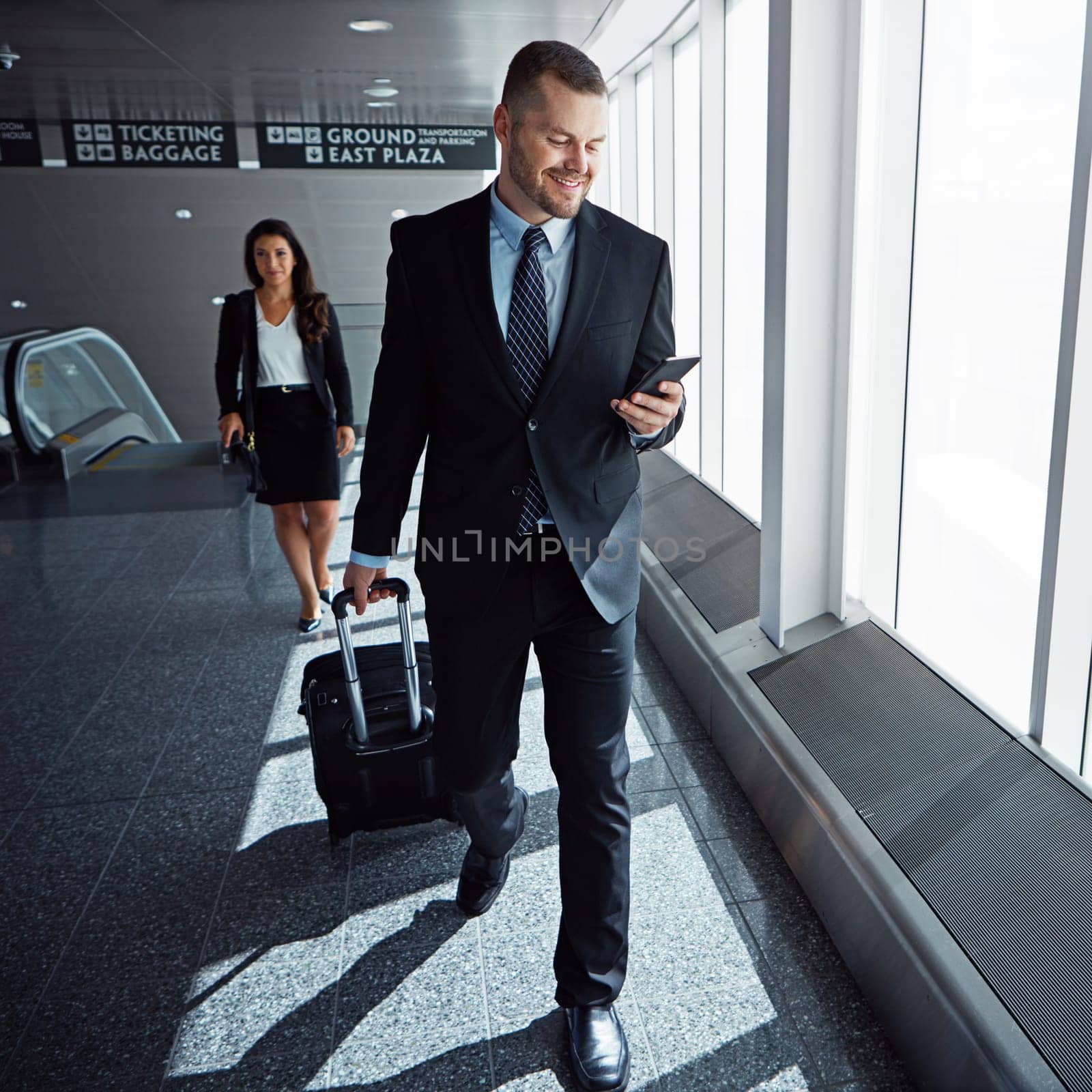 Business man, smartphone and suitcase in airport hallway with smile, thinking or idea for international travel. Entrepreneur, luggage and phone with flight schedule for global immigration in London by YuriArcurs