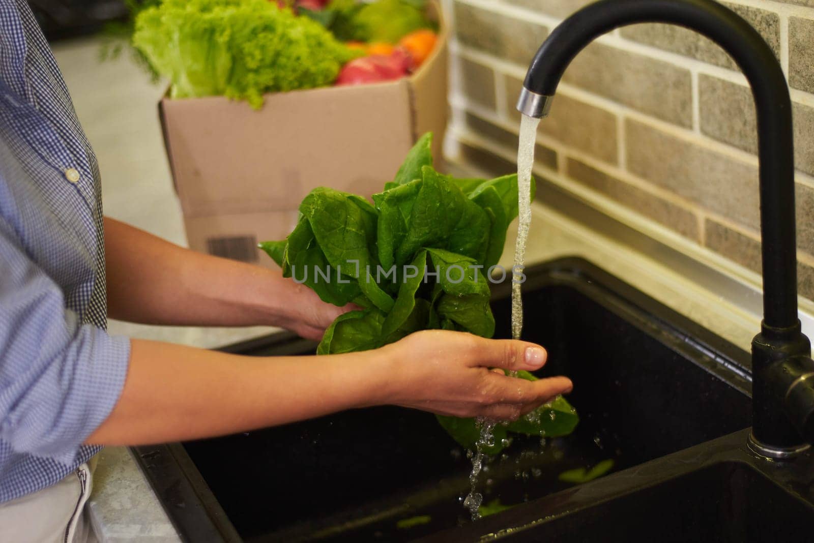 Close-up view of the hands of a housewife woman washing vegetables and greens in the kitchen at home, preparing healthy salad for dinner. Healthy food, proper nutrition and homemade food concept.