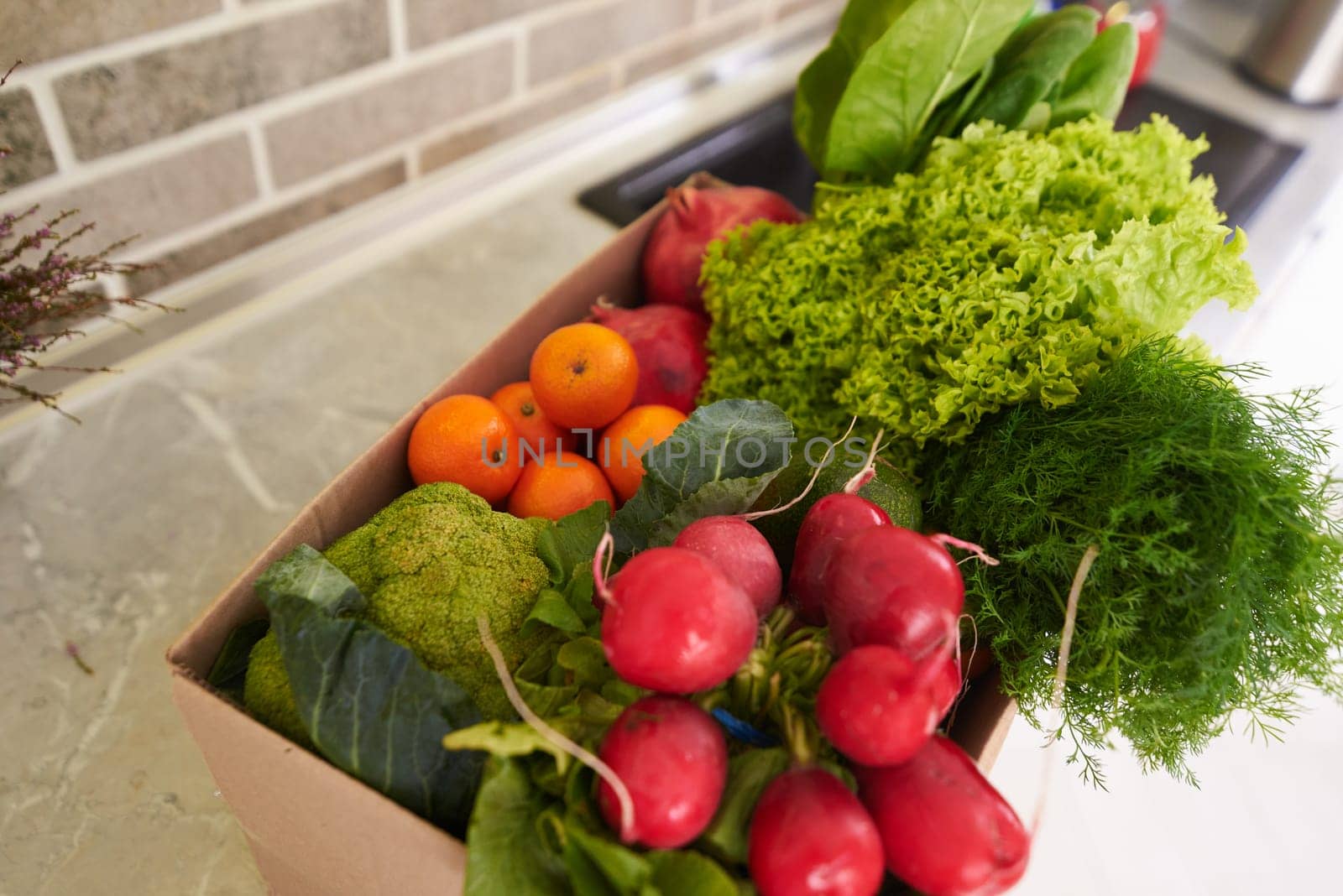 Top view of a recyclable cardboard box with fresh organic crop of fruits, vegetables and greens on the kitchen counter. Sustainable lifestyle. Healthy food and lifestyle. Slimming and diet concept