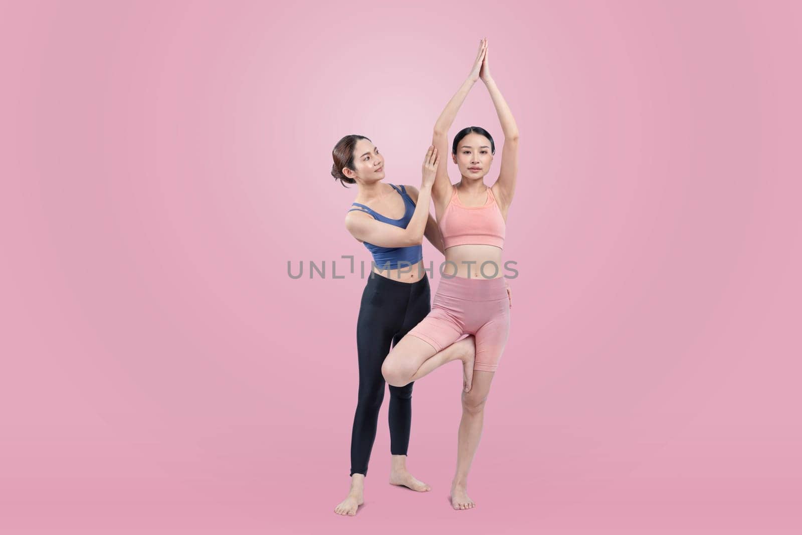 Asian woman in sportswear doing yoga exercise in standing pose with her trainer or yoga buddy. Healthy body care and meditation yoga lifestyle in full shot on isolated background. Vigorous