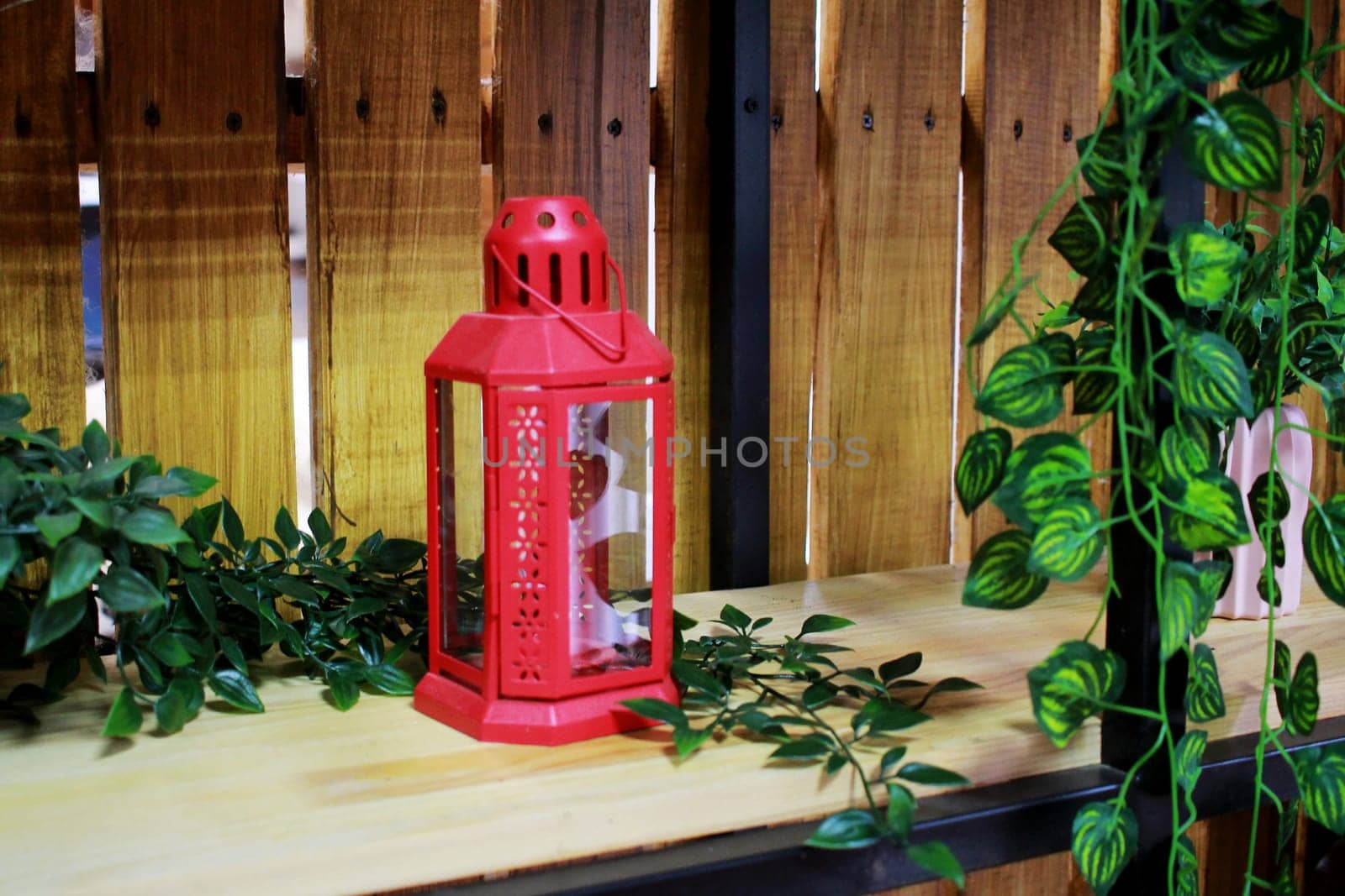 Photo a red candlestick on the shelf of a wooden rack. Decorative artificial plants. Comfort.