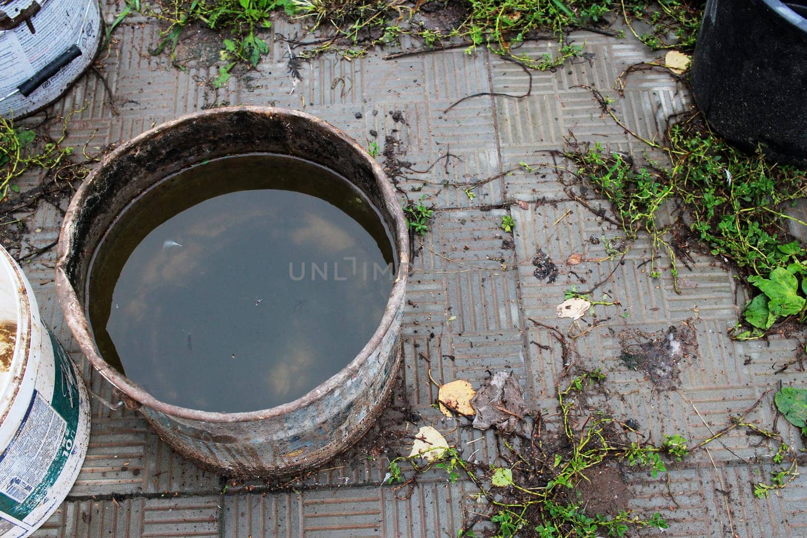 Photo a container with rainwater in the country after the rain. Mud.Plastic bucket and paving slabs.