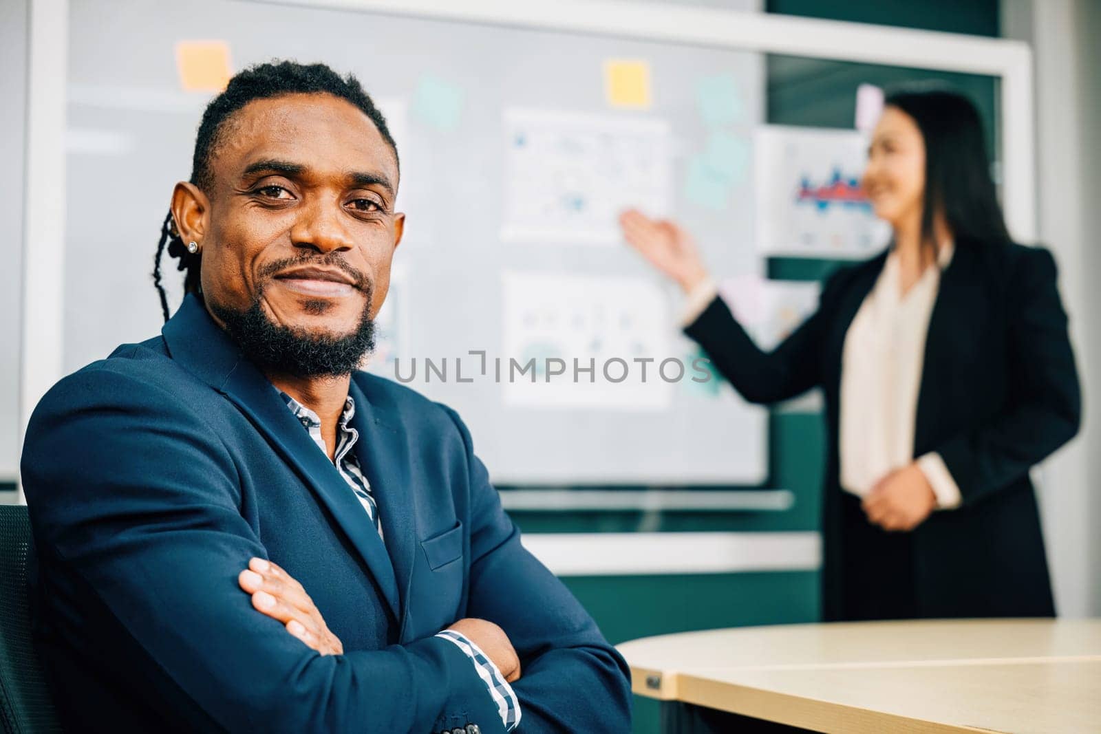 Confident and successful, black businessman, CEO and leader, is at team meeting in an office. He smiles, reflecting leadership in a diverse workplace. A portrait of excellence in corporate leadership. by Sorapop