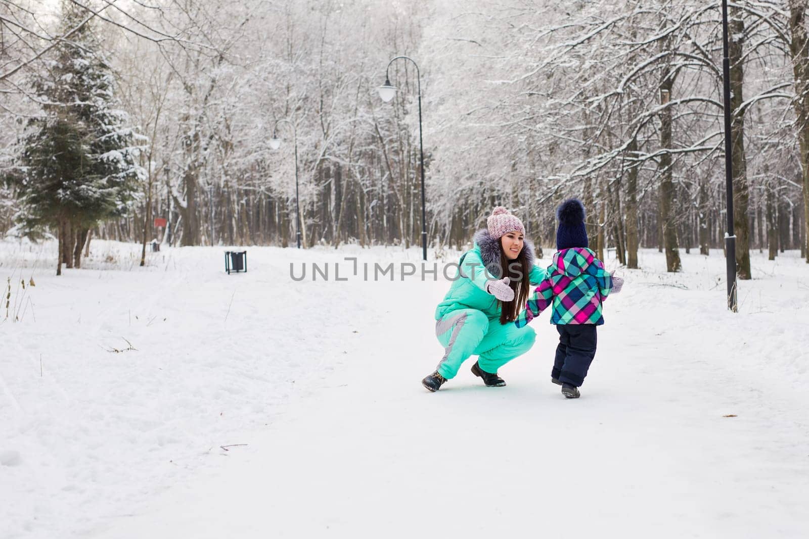 happy family mother and baby girl daughter playing and laughing in winter outdoors in the snow