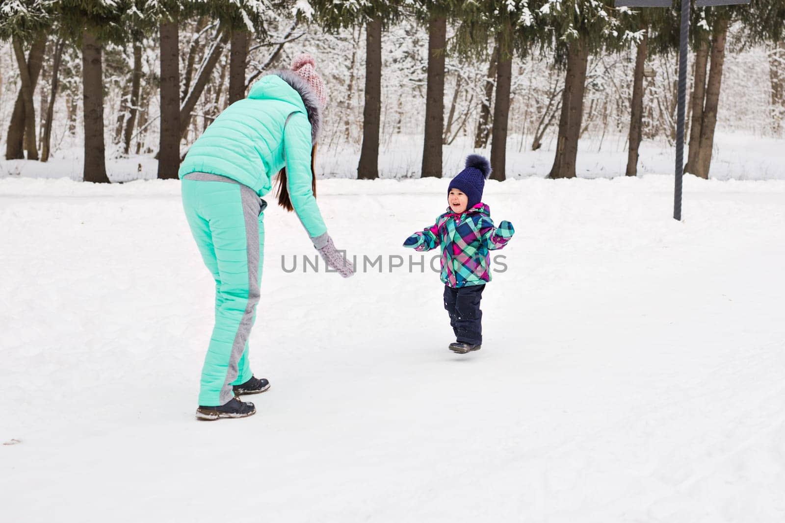 happy family mother and baby girl daughter playing and laughing in winter outdoors in the snow