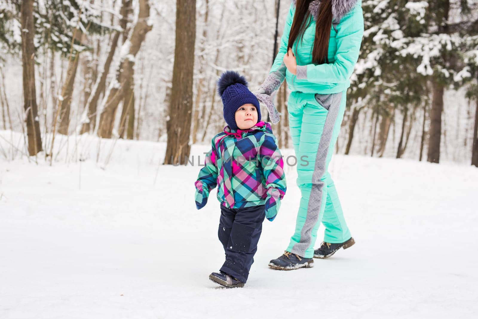 happy family mother and baby girl daughter playing and laughing in winter outdoors in the snow