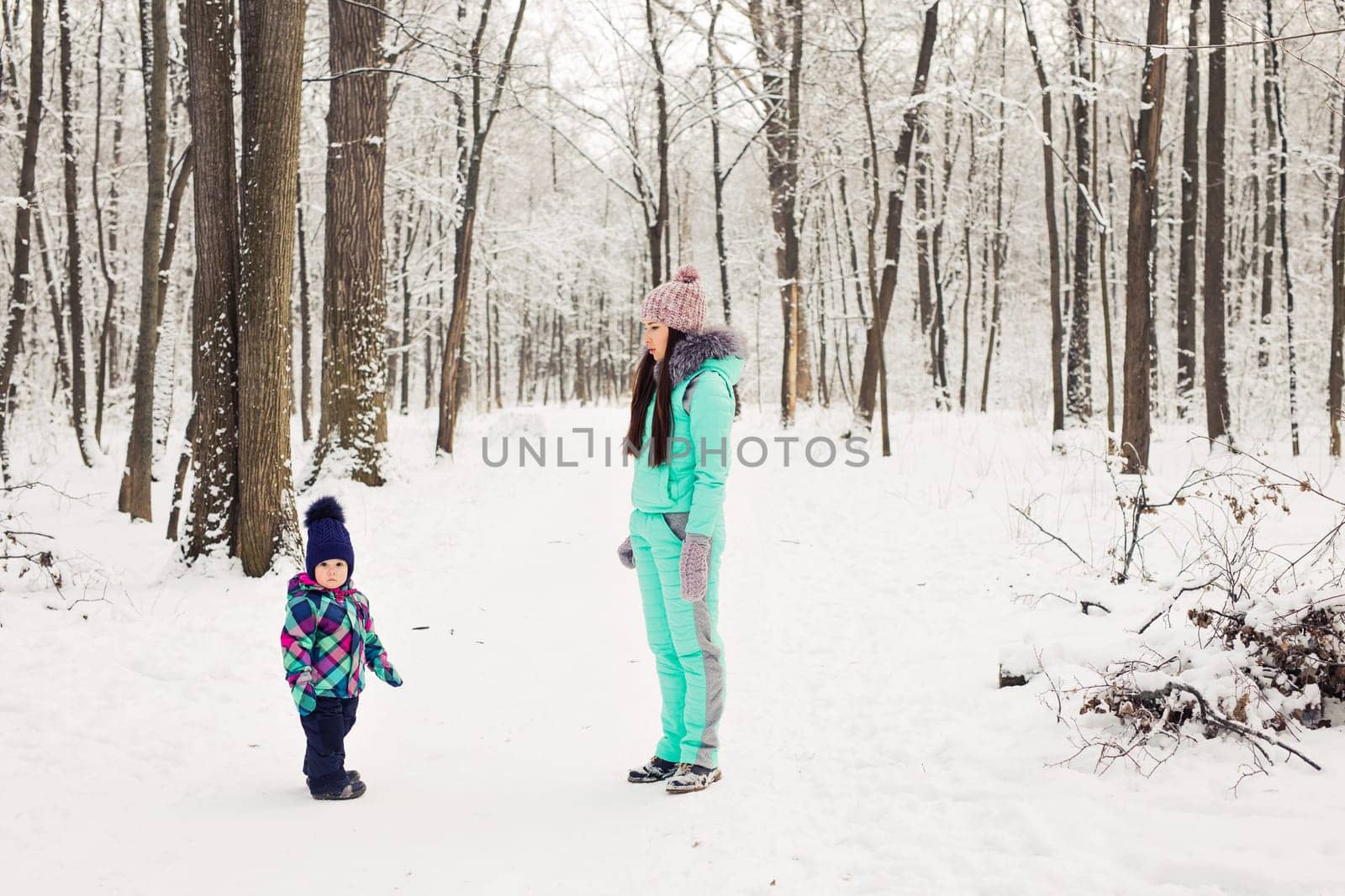 happy family mother and baby girl daughter playing and laughing in winter outdoors in the snow