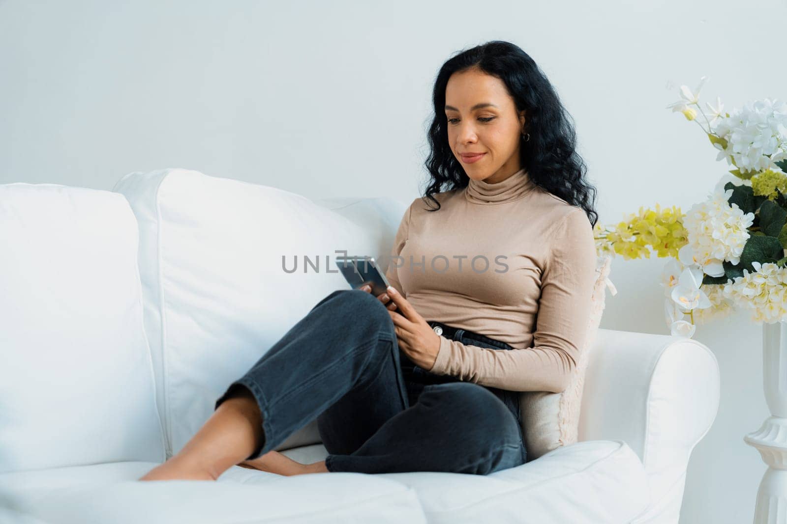 Relaxed young African American woman using crucial mobile phone on sofa couch in living room at home