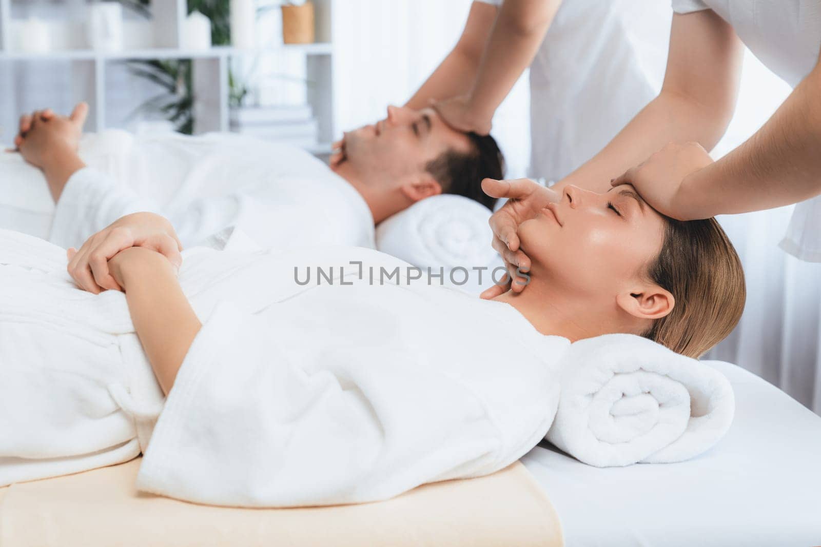 Caucasian couple enjoying relaxing anti-stress head massage and pampering facial beauty skin recreation leisure in dayspa modern light ambient at luxury resort or hotel spa salon. Quiescent