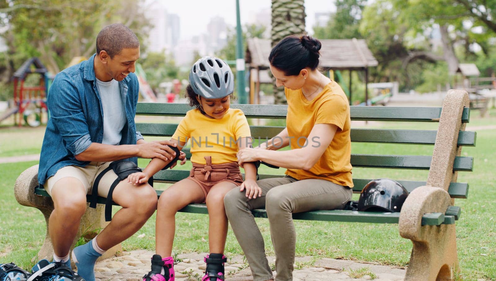 Parents, park bench and helmet with kid, help and safety for skating, rollerskate or bike. Interracial family, mom and dad with helping hand, teaching and girl kid for bonding, learning and exercise.