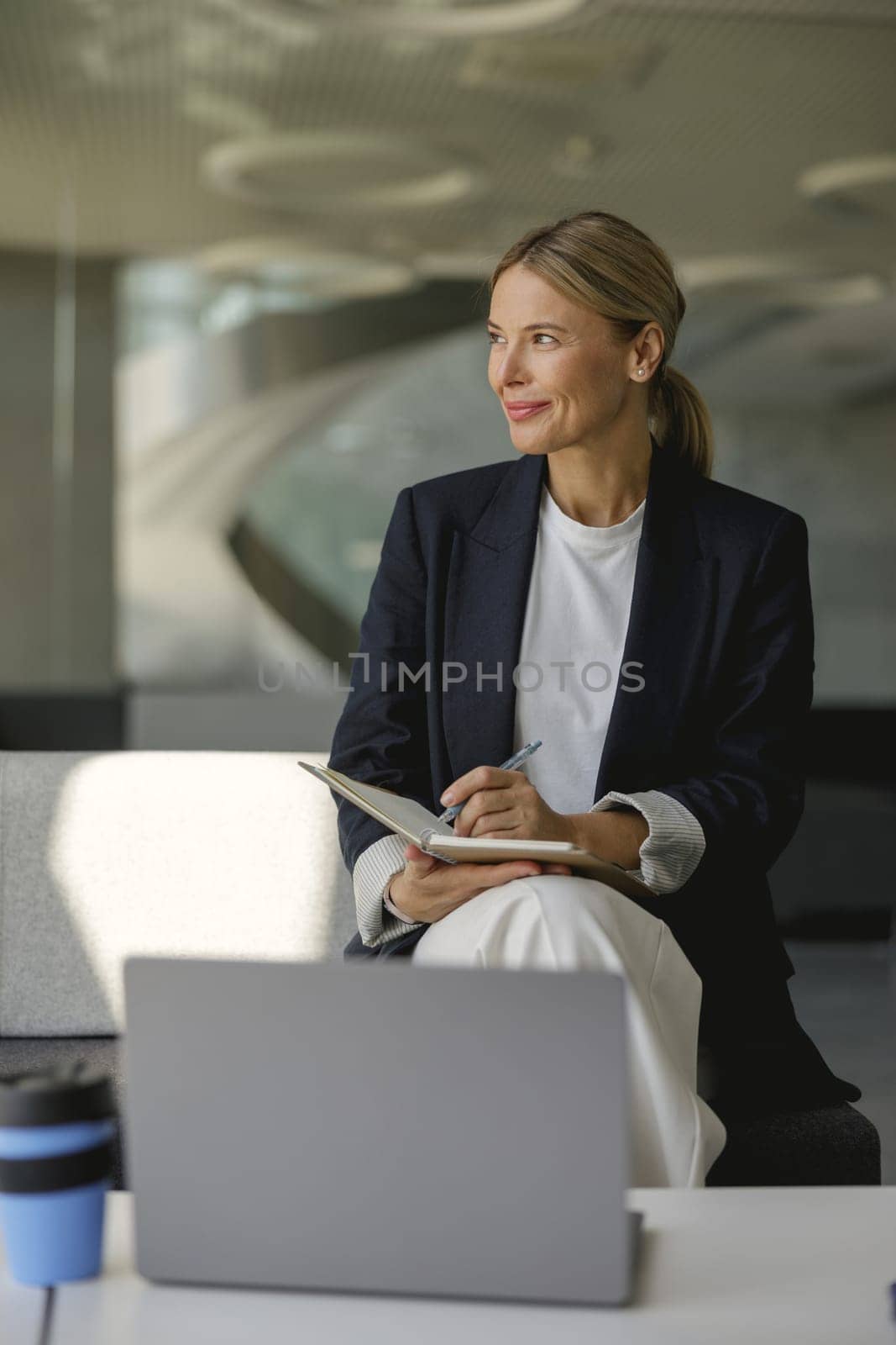 Confident female manager making notes in note pad sitting on modern office background by Yaroslav_astakhov