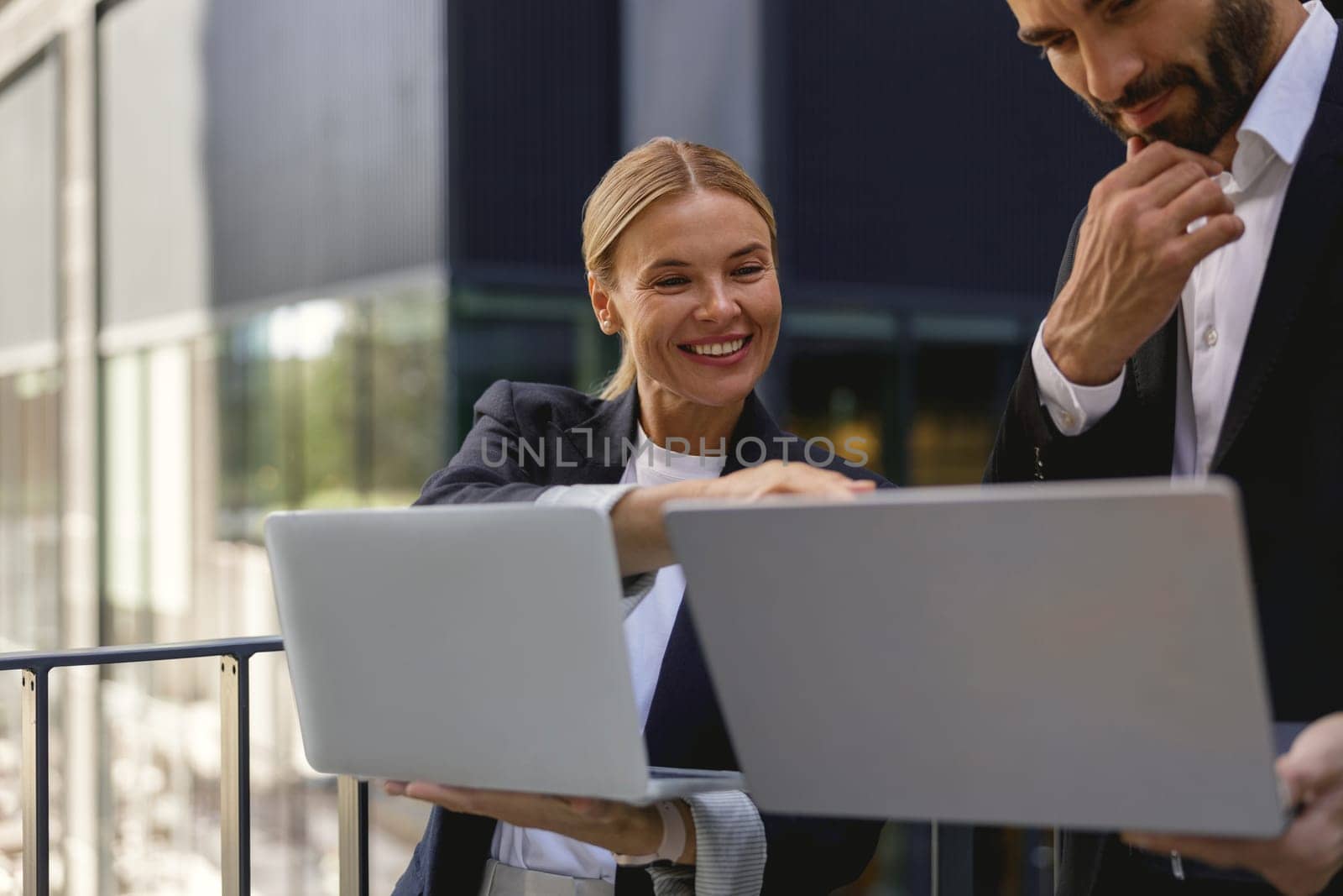 Two business people discuss biz issue while use laptop standing on modern office terrace