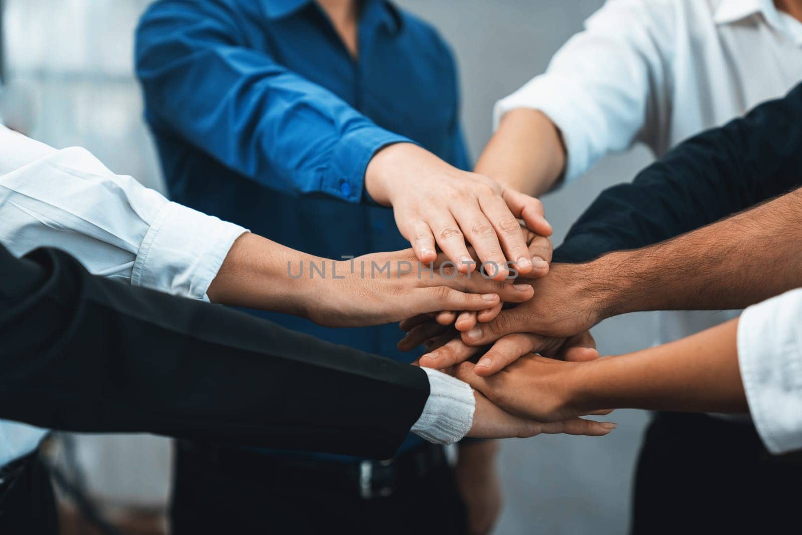 Group of diverse office worker join hand together in office room symbolize business synergy and strong productive teamwork in workplace. Cooperation and unity between business employee. Prudent