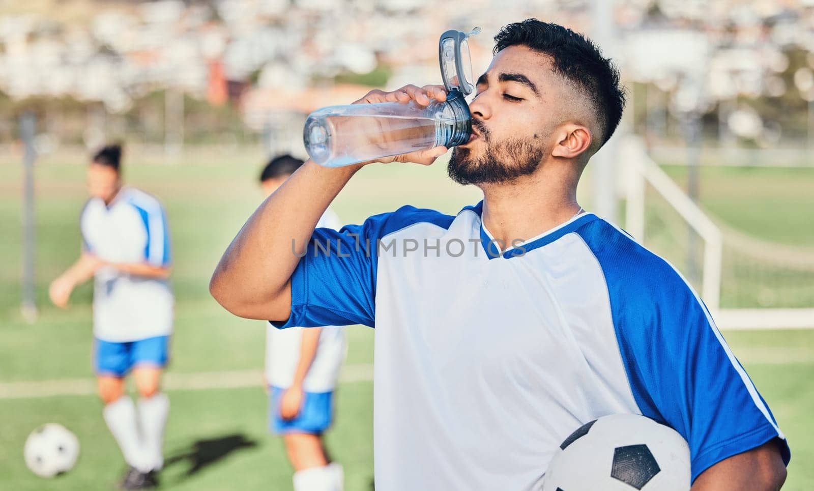 Football, athlete and man drinking water outdoor on a sports field for fitness competition. Tired male soccer player on a break and exhausted from exercise, challenge or training workout for health.