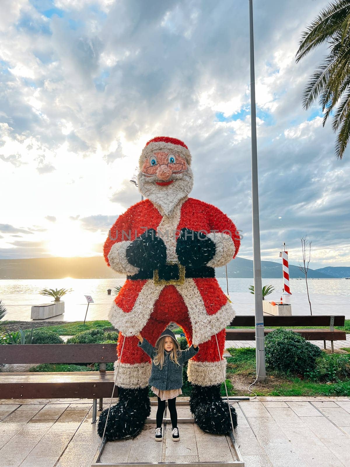 Little girl stands near the figure of Santa Claus on the promenade by the sea. High quality photo
