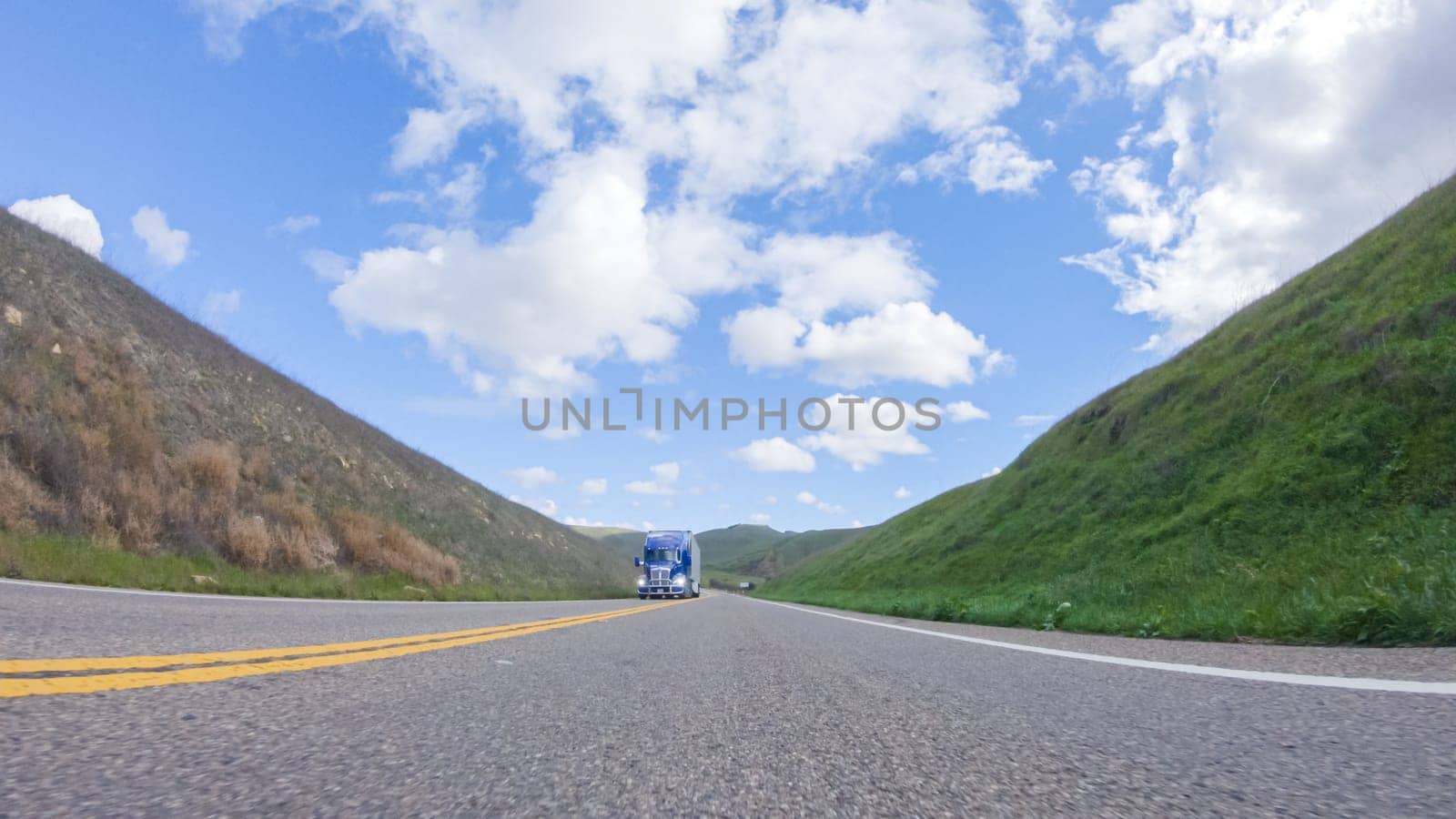 On a clear winter day, a car smoothly travels along Highway 101 near Santa Maria, California, under a brilliant blue sky, surrounded by a blend of greenery and golden hues.