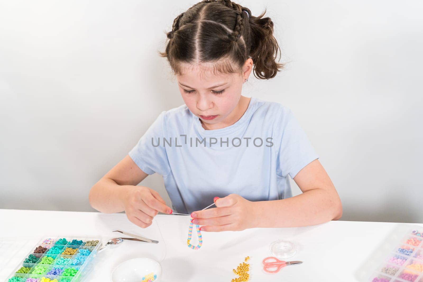 Little girl enjoys crafting colorful bracelets with vibrant clay beads set.