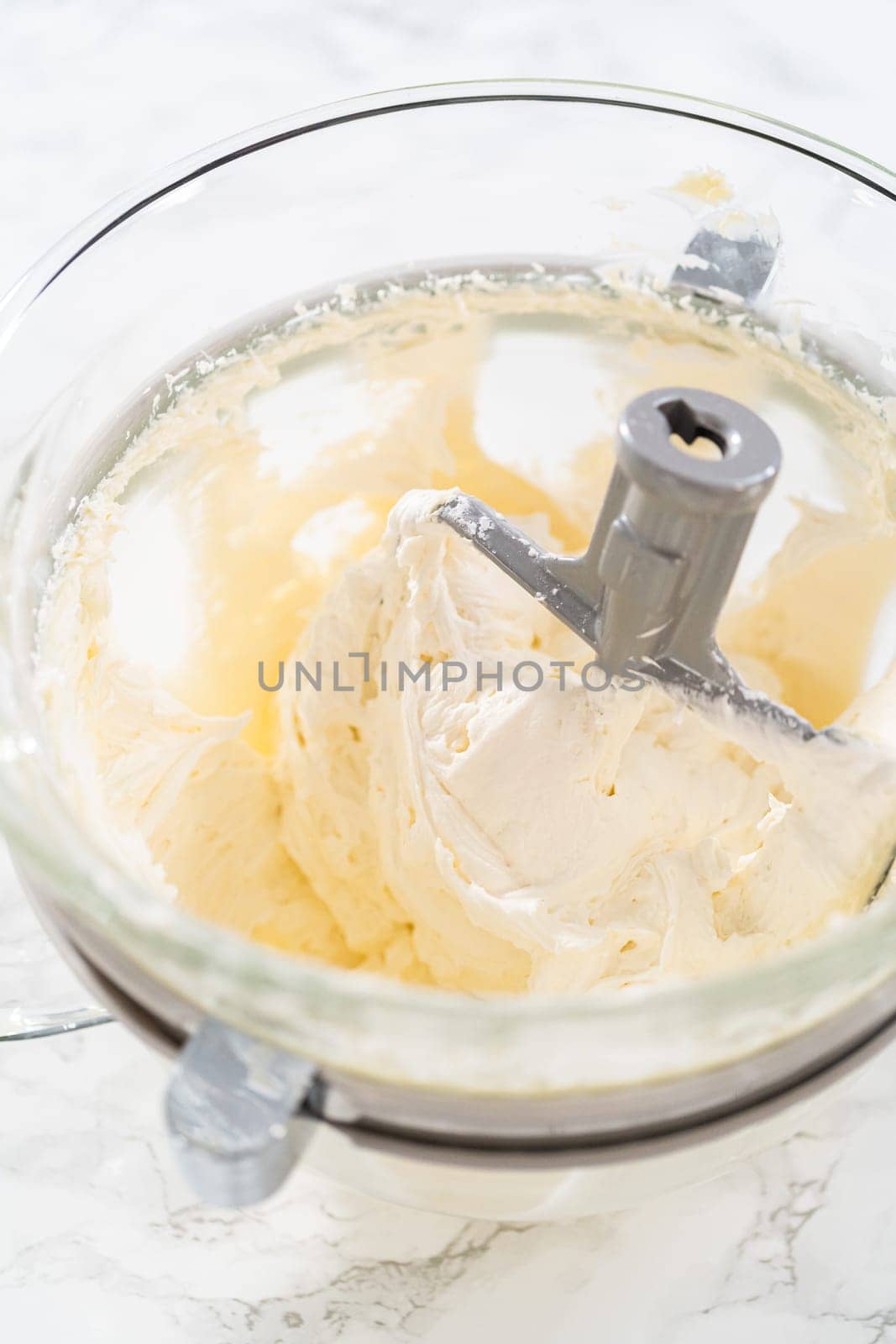 Whisking buttercream frosting in a glass mixing bowl with an electric kitchen mixer for American flag mini cupcakes.