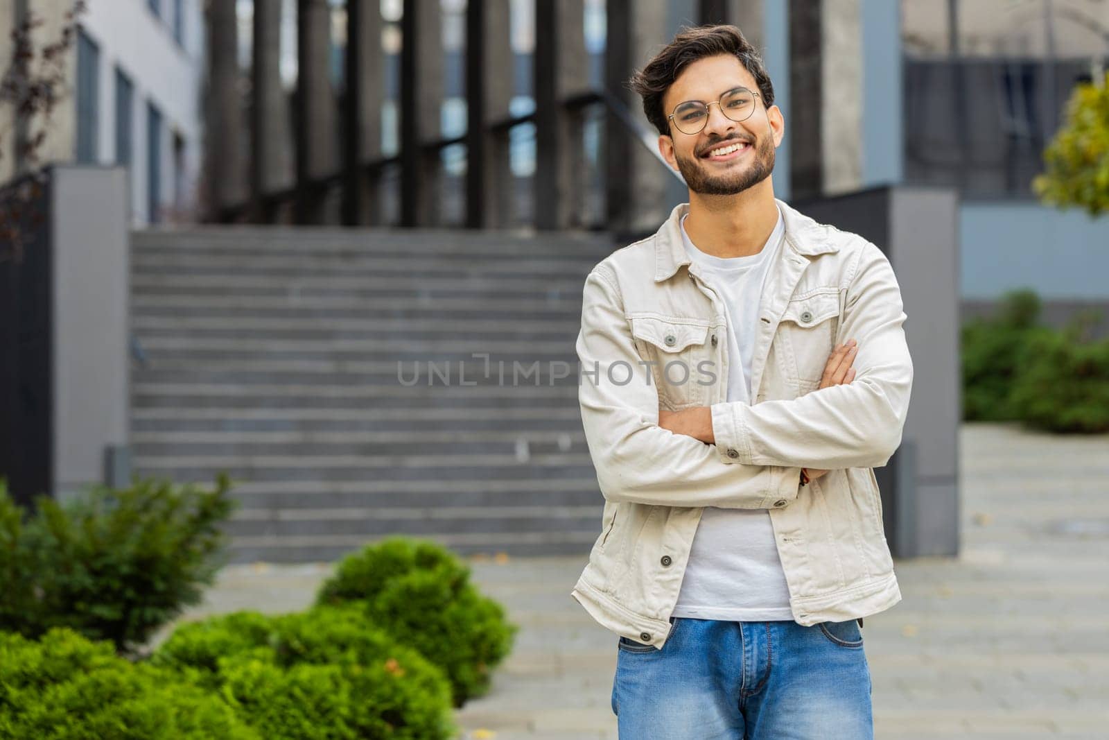 Portrait of happy Indian man smiling friendly, glad expression looking at camera dreaming, resting relaxation feel satisfied good news outdoors. Arabian guy in city street. Business people. Copy-space