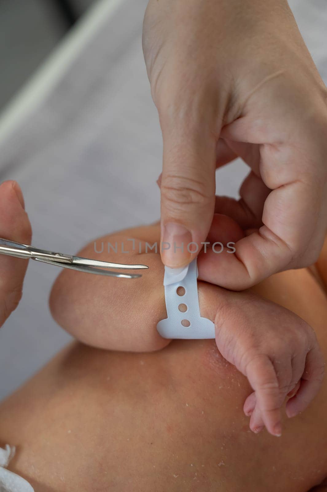 A woman cuts a tag from a newborn boy's hand with nail scissors. Close-up of hands. by mrwed54