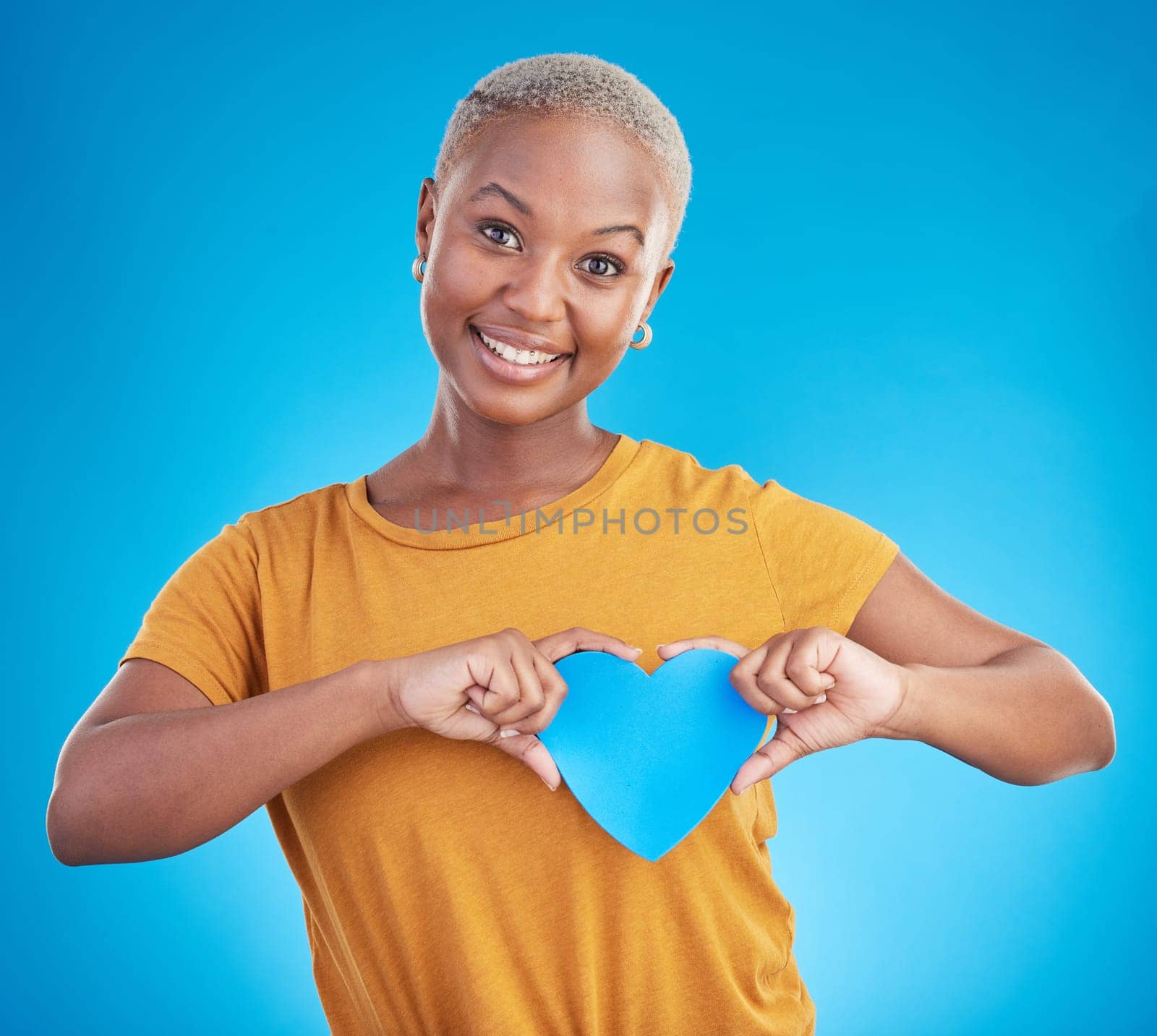 Portrait, love and heart with a black woman on blue background in studio for health or wellness. Smile, emoji and social media with a happy young person looking excited for romance or valentines day.