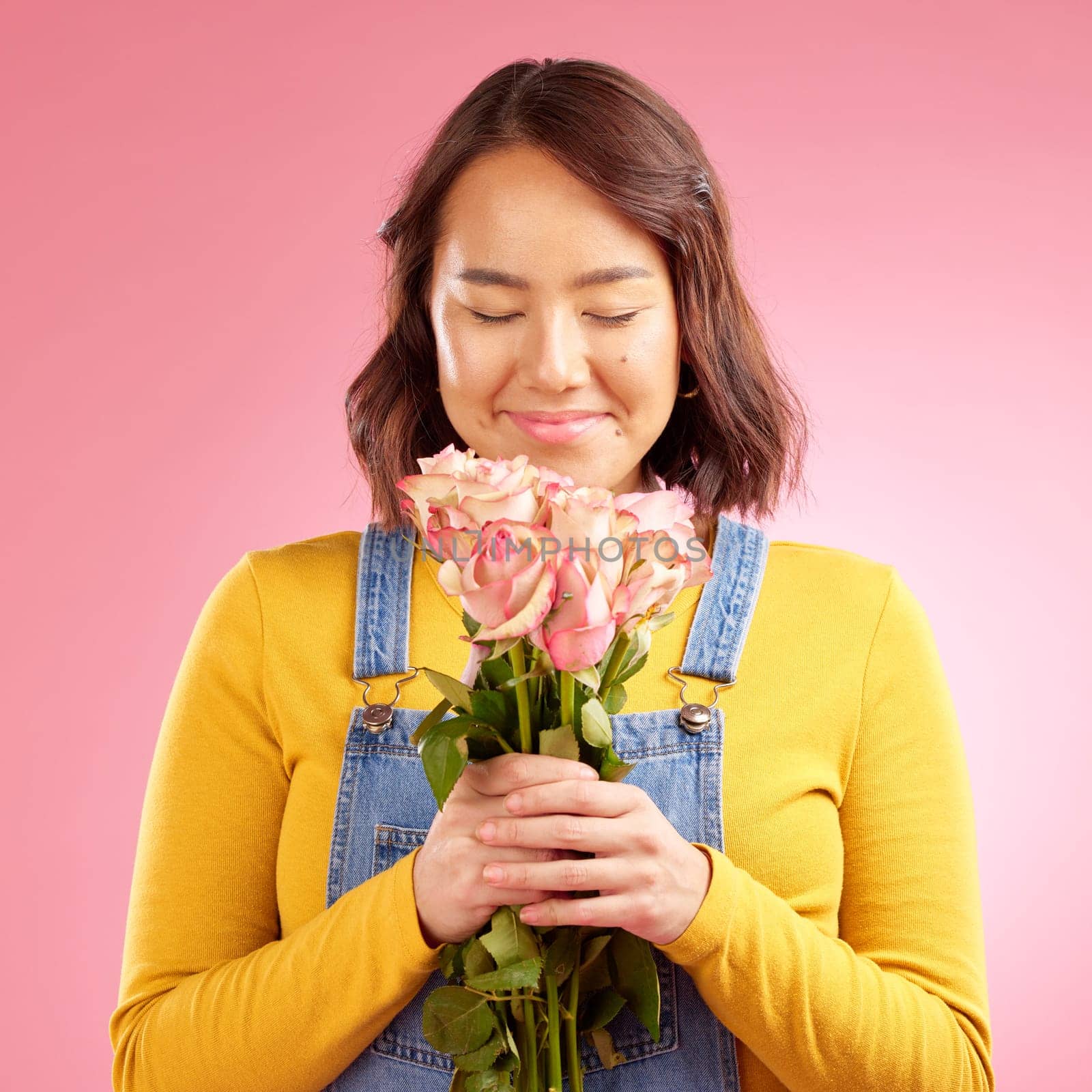 Woman, smell roses and gift in studio, smile and excited for celebration, birthday or party by pink background. Japanese student girl, thinking and bouquet of flowers for present, reward or romance by YuriArcurs