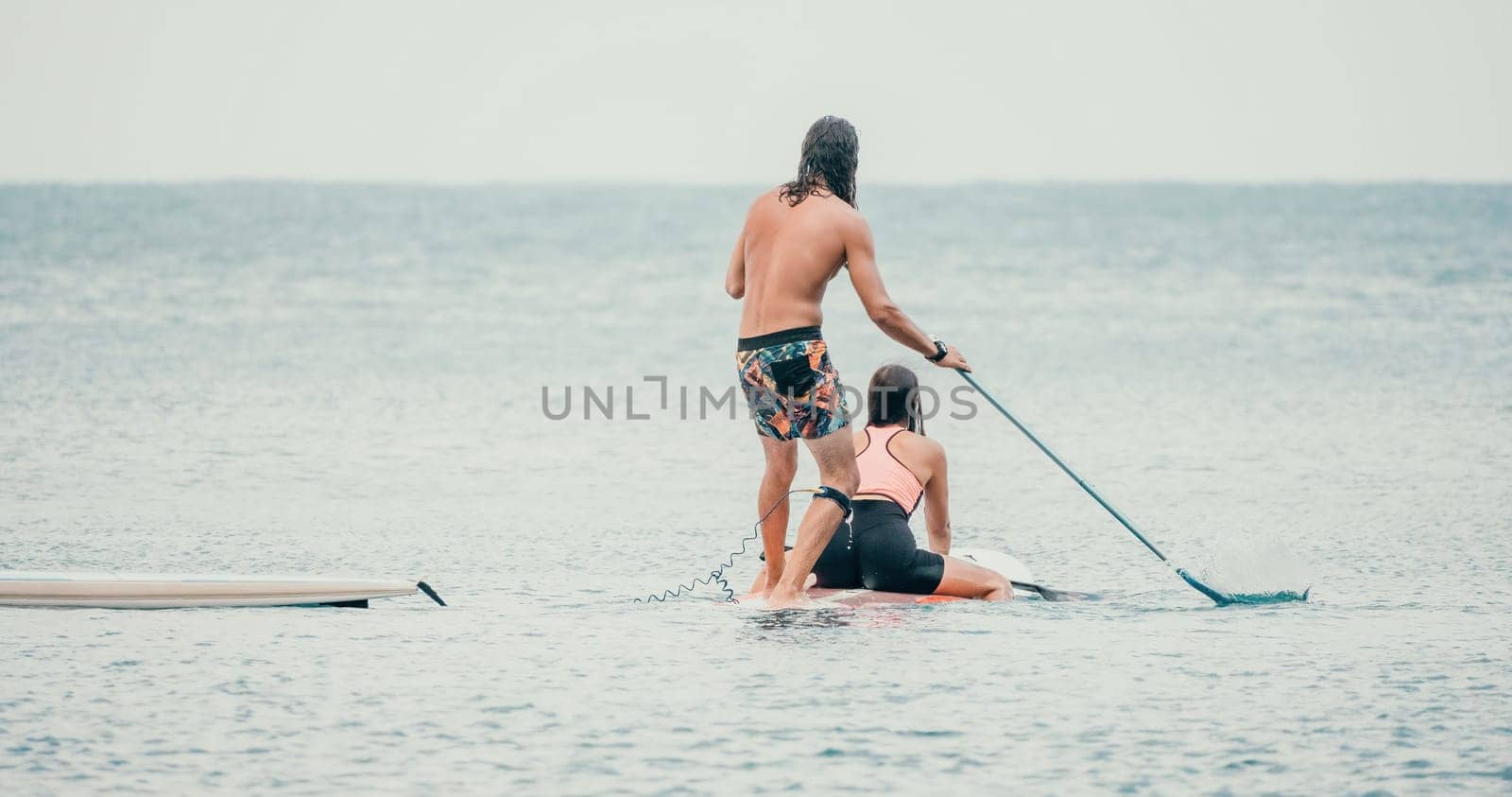 Sea woman and man on sup. Silhouette of happy young woman and man, surfing on SUP board, confident paddling through water surface. Idyllic sunset. Active lifestyle at sea or river