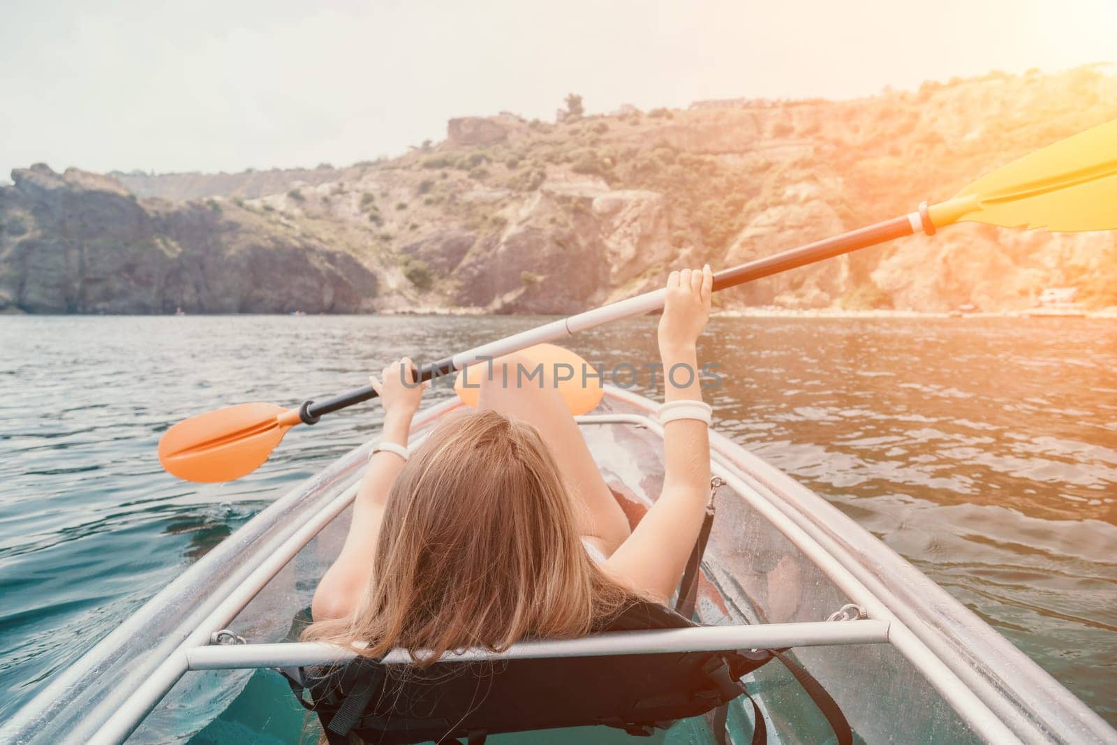 Woman in kayak back view. Happy young woman with long hair floating in transparent kayak on the crystal clear sea. Summer holiday vacation and cheerful female people having fun on the boat.