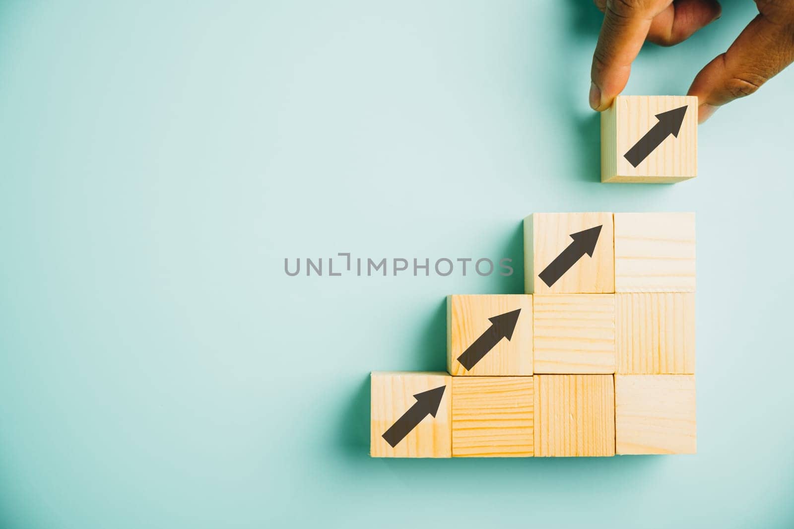 Male hands arranging stacked wooden blocks as steps on a white table. Business growth concept with an arrow pointing upwards, symbolizing future development and achieving goals. Copy space available.