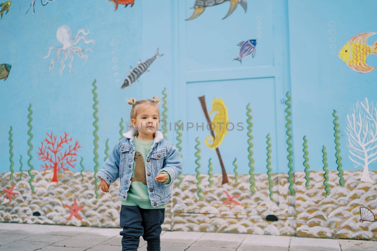 Little girl walks near a house painted with colorful drawings. High quality photo