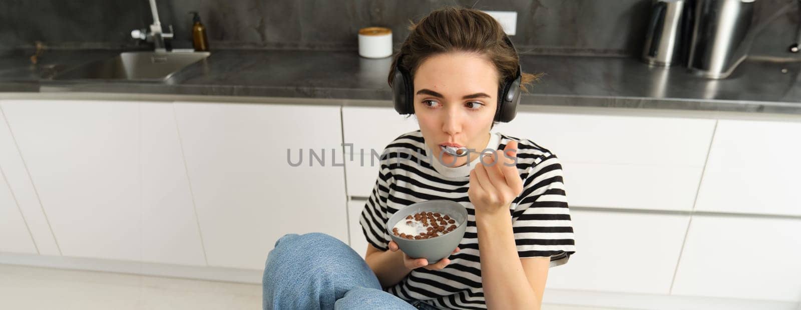 Portrait of carefree brunette woman, eating her cereals, listening to music, having breakfast in the kitchen.