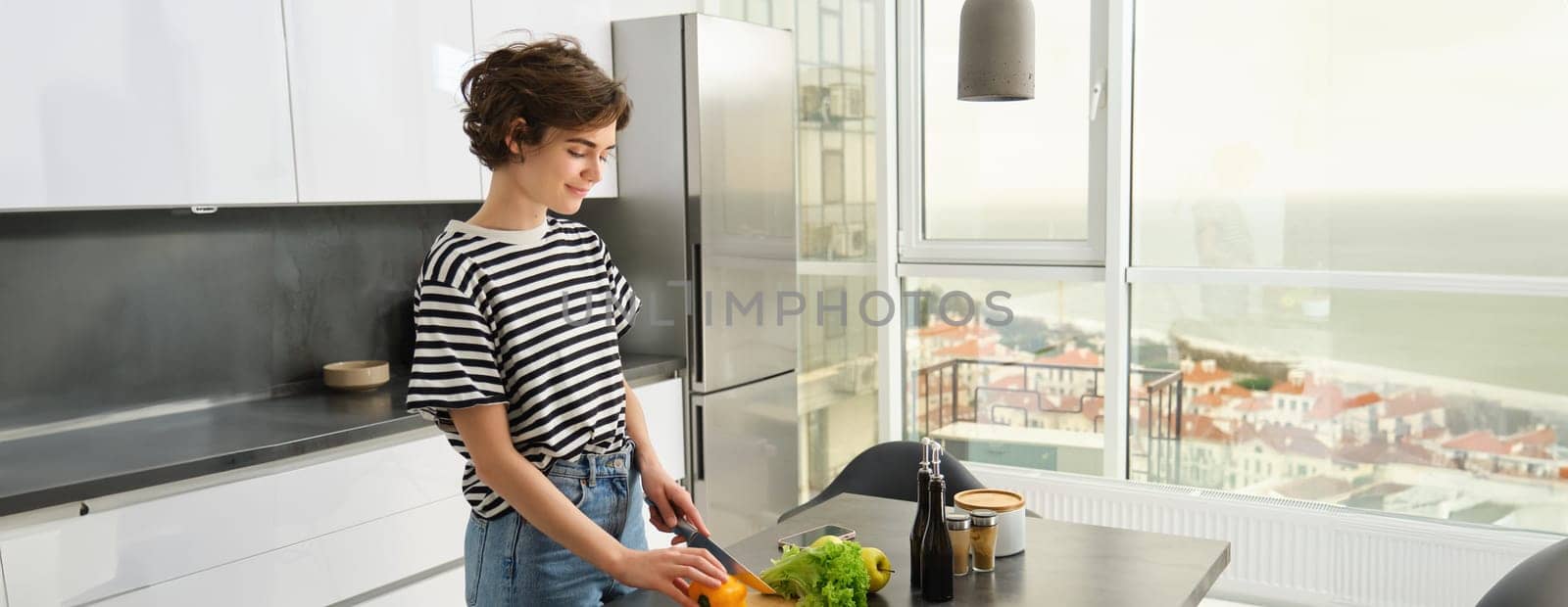 Portrait of young woman cooking salad. Cute girl vegan chopping vegetables on kitchen counter, preparing food by Benzoix