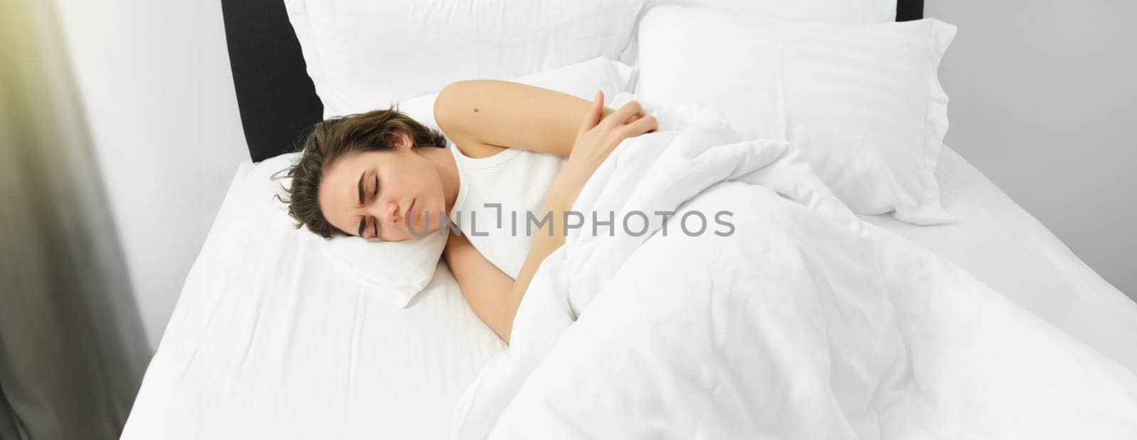 Portrait of woman lying in bed with stomach ache, has menstrual cramps, frowning and feeling pain period. Wellbeing and health concept