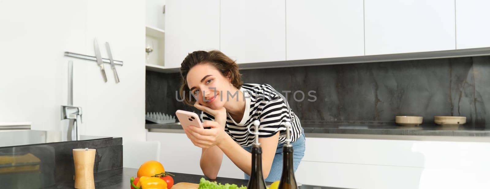 Portrait of woman, lifestyle blogger, posting picture of her cooking process on smartphone app, standing near vegetables and chopping board by Benzoix