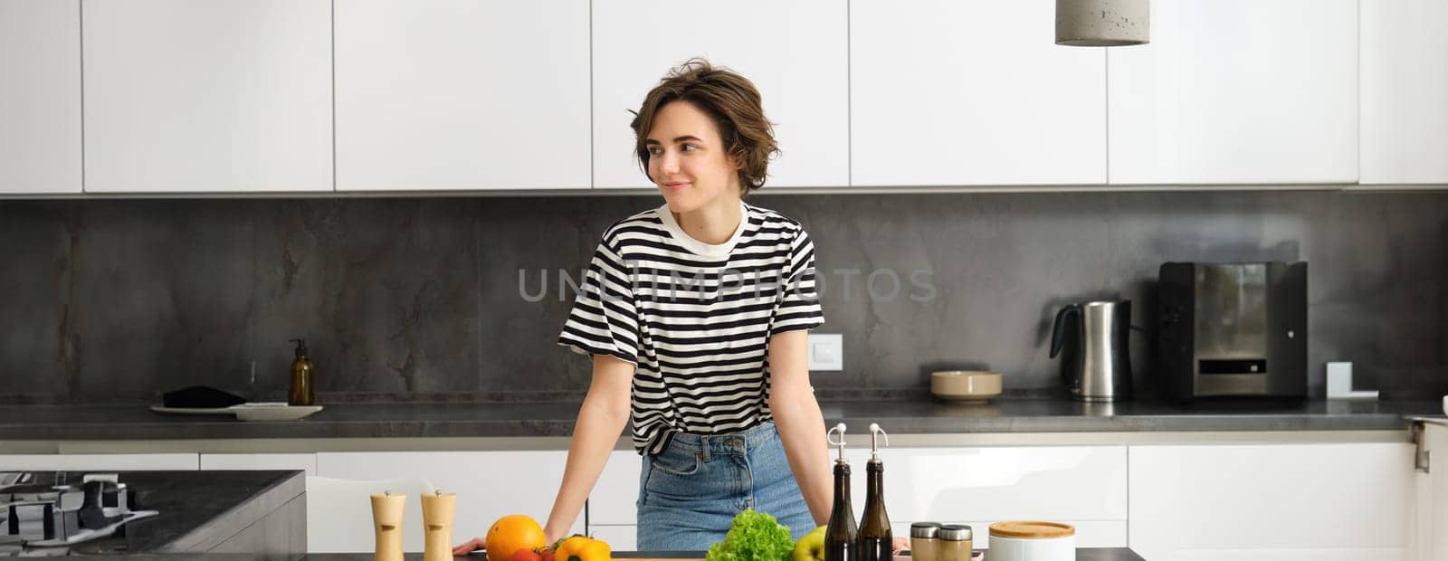 Portrait of smiling cute young woman making breakfast, chopping vegetables in the kitchen, preparing vegan meal.