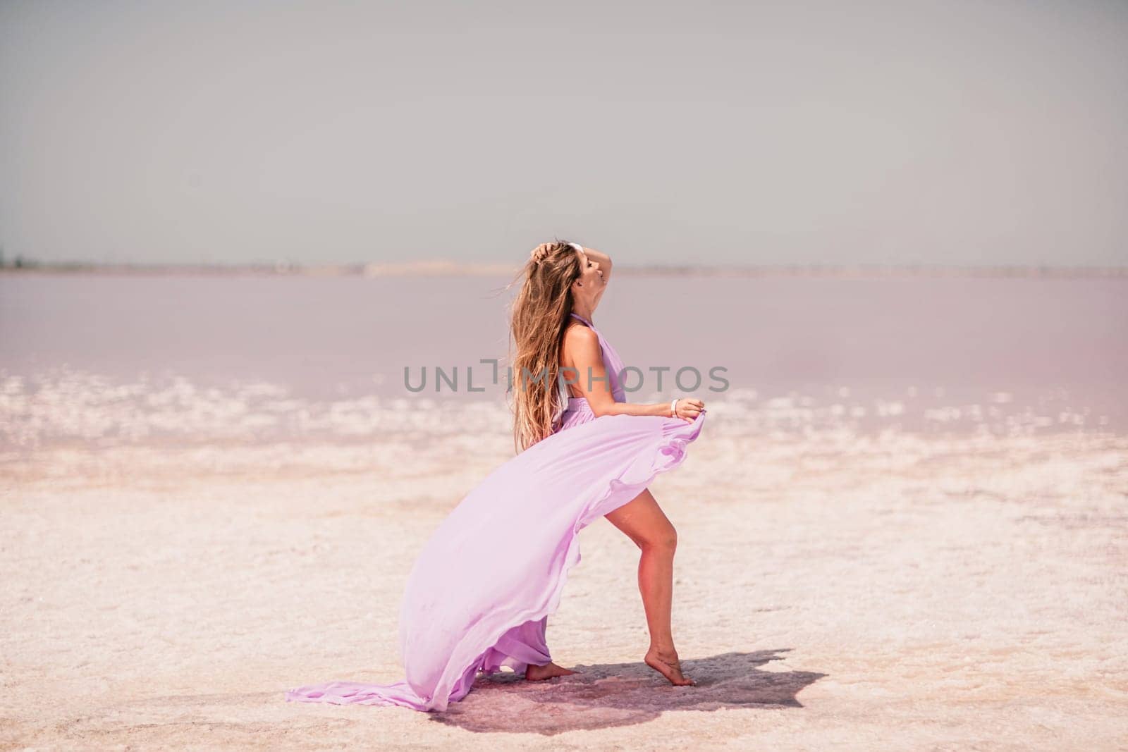 Woman pink salt lake. Against the backdrop of a pink salt lake, a woman in a long pink dress takes a leisurely stroll along the white, salty shore, capturing a wanderlust moment