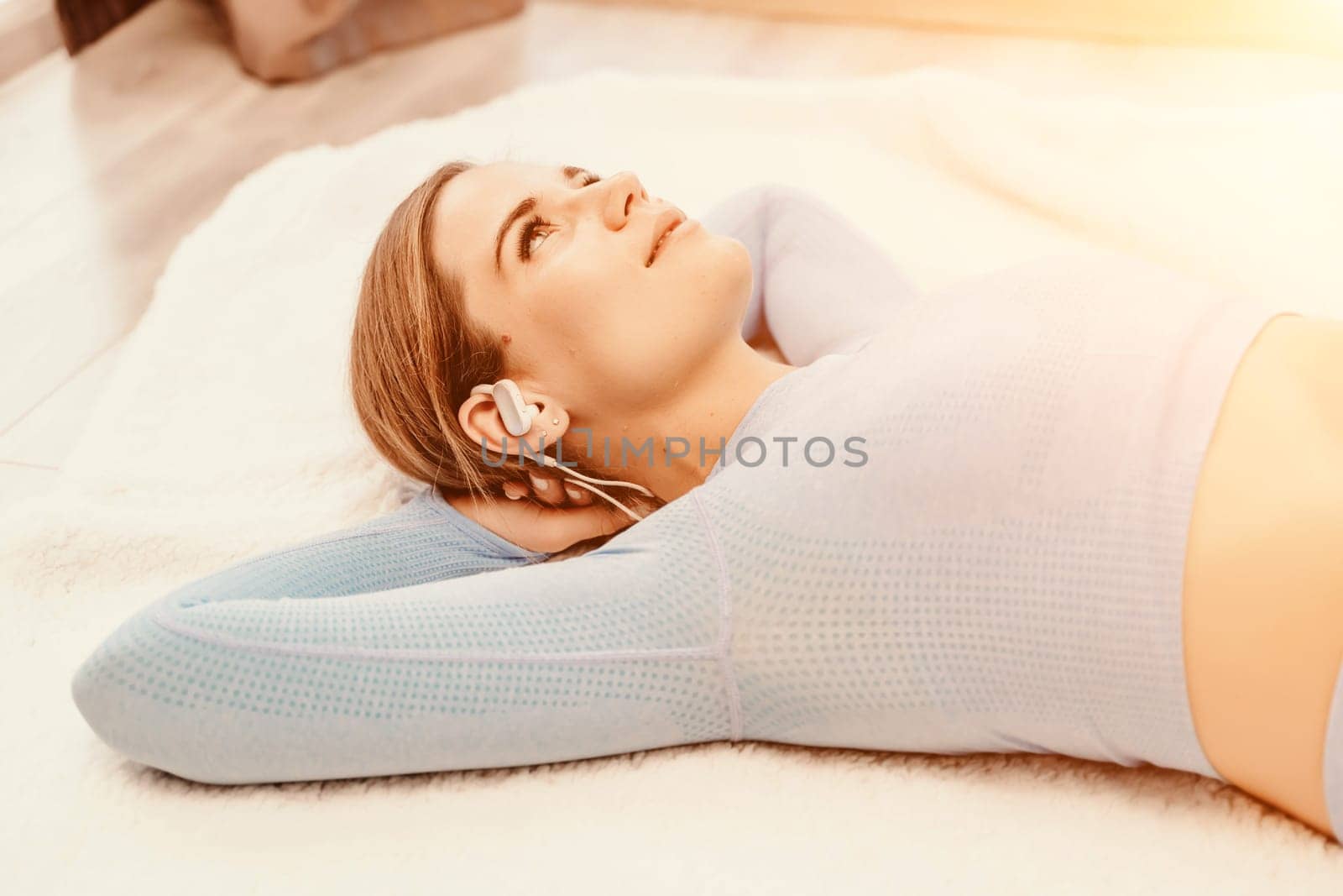 Top view portrait of relaxed woman listening to music with headphones lying on carpet at home. She is dressed in a blue tracksuit