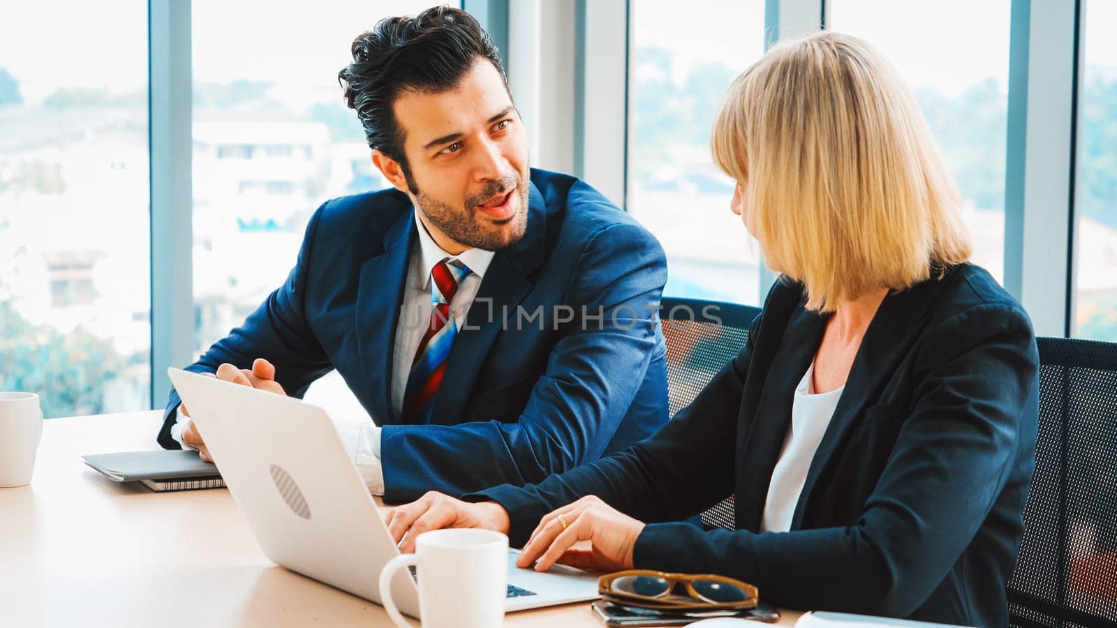 Two business people talk project strategy at office meeting room. Businessman discuss project planning with colleague at modern workplace while having conversation and advice on financial report. Jivy