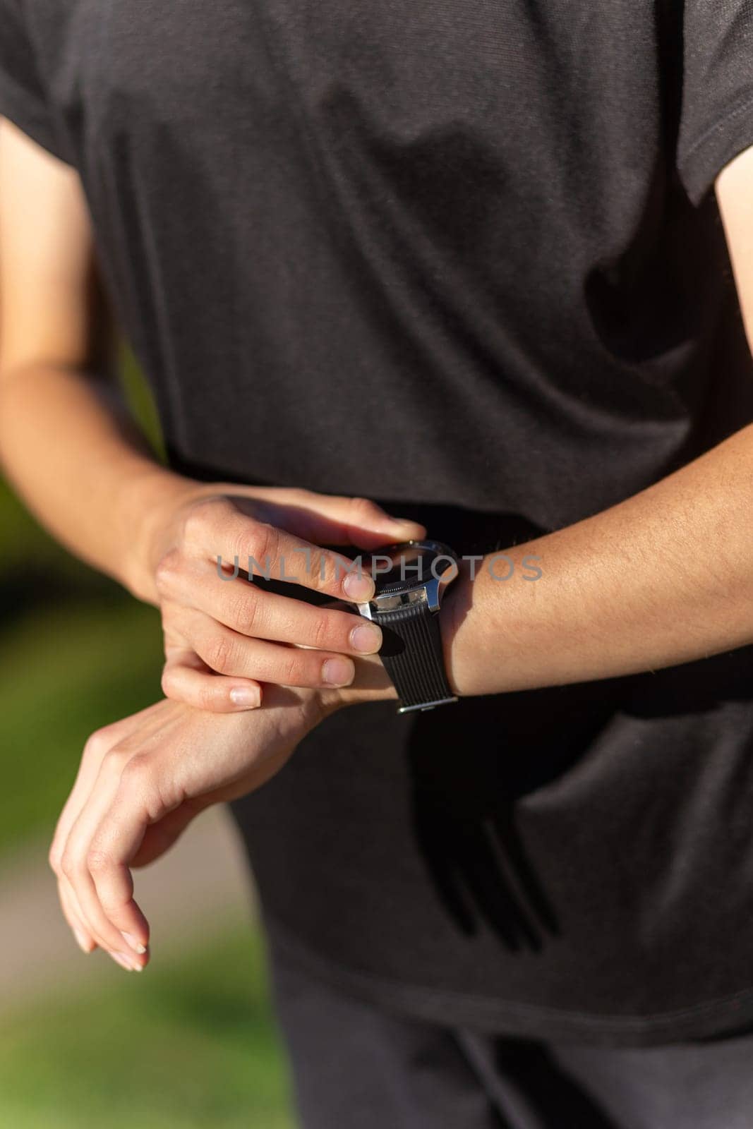 Teenage girl in black clothes checking her fitness watch after a workout. Tired runner girl controlling pulsations checking smartwatch.