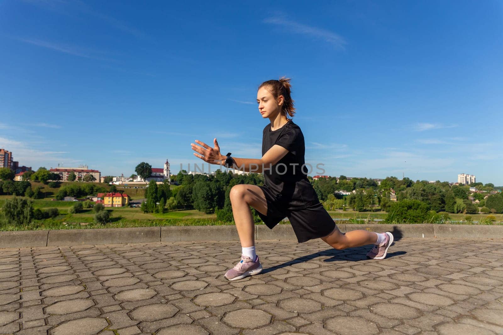 Young, fit and sporty girl in black clothes stretching after the workout in the urban city park. Fitness, sport, urban jogging and healthy lifestyle concept.