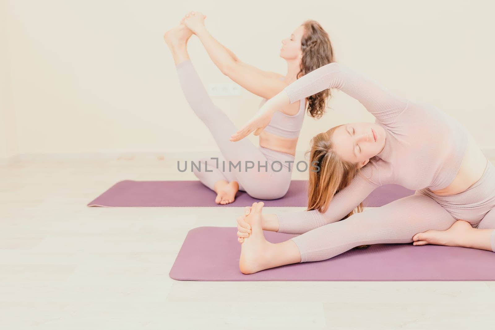 Well looking middle aged sporty woman, fitness instructor in pink sportswear doing stretching and pilates on yoga mat in the studio with mirror. Female fitness yoga. Healthy lifestyle and harmony. by panophotograph
