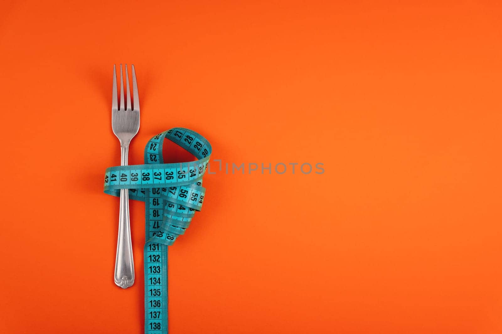 Measuring tape threaded through a fork on an orange background. Good healthy nutrition. Therapeutic fasting. Diet for weight loss concept by yanik88