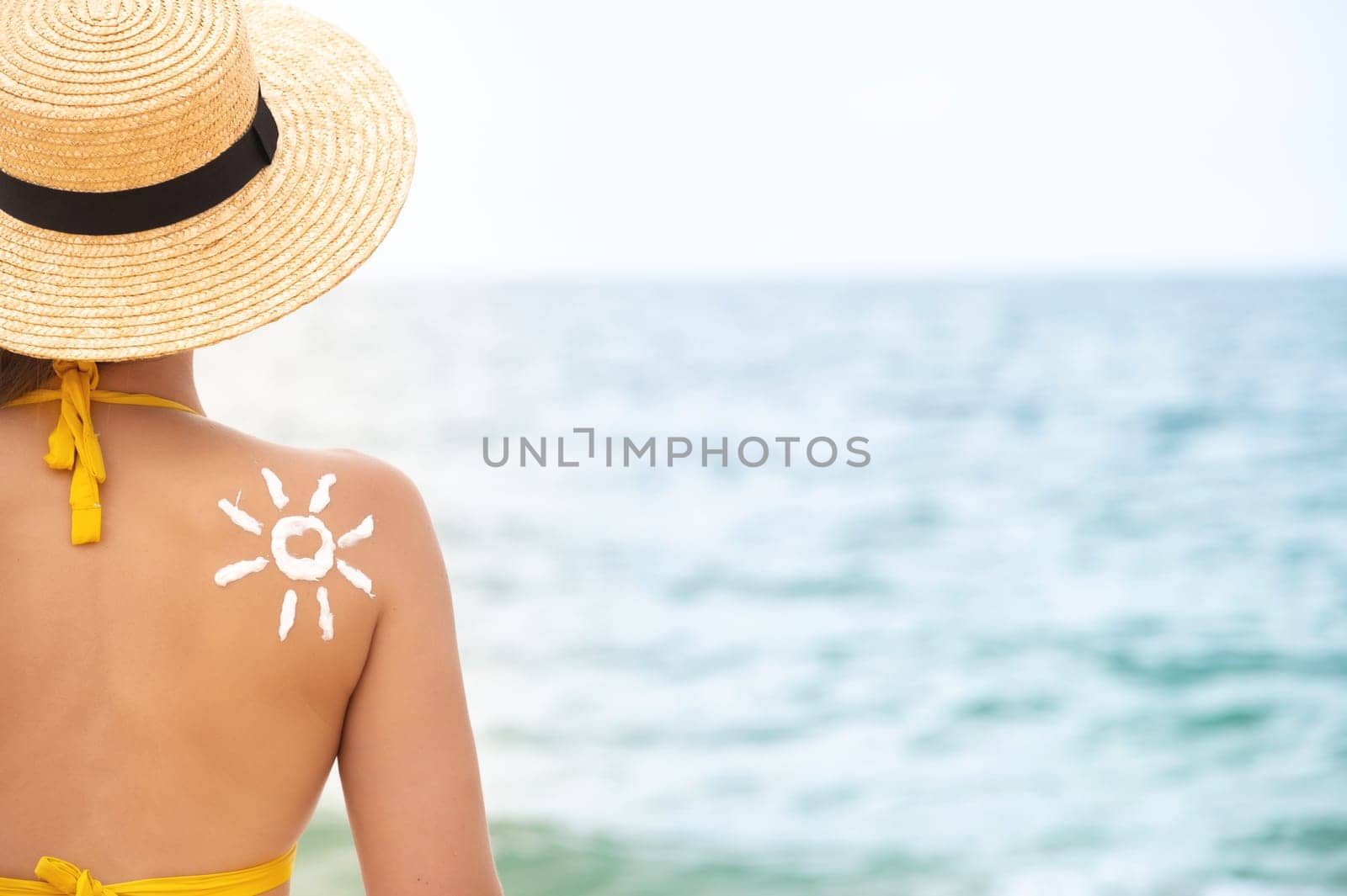 A woman applied sunscreen to her tanned shoulder in the shape of a sun. Sun protection. Sunscreen. Skin and body care